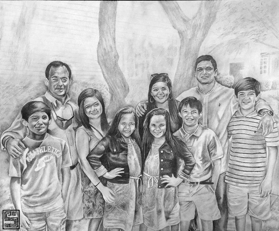 A group of ten people, including children and adults, smiling and posing outdoors with trees in the background.