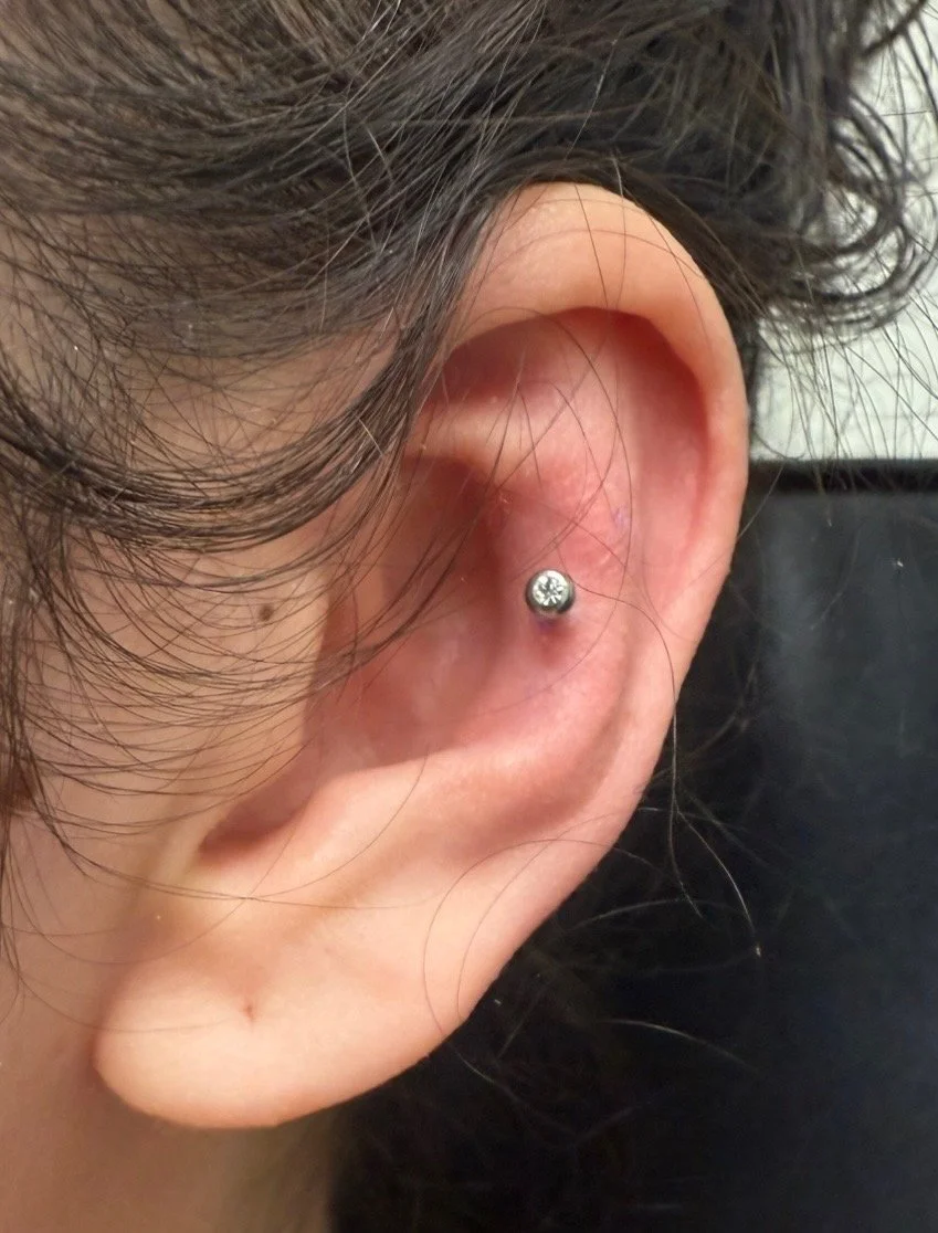Close-up of a human ear with a small, round, clear gemstone stud earring in the upper part of the earlobe.