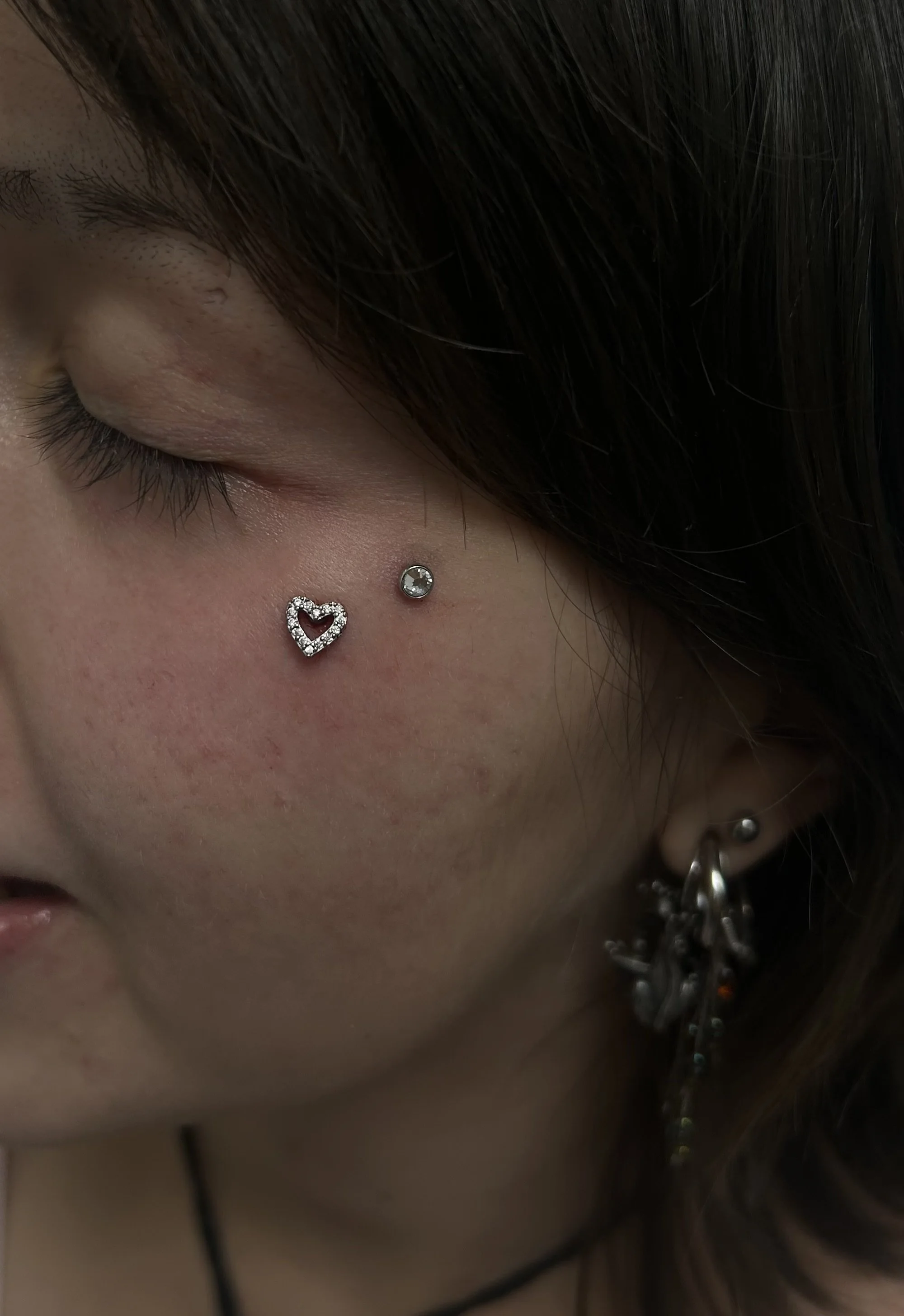 Close-up of a person's face, focusing on their closed eye, earrings, and hair.