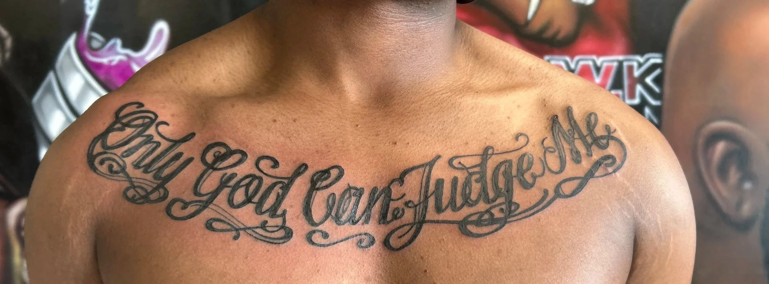 Close-up of a person's chest with a tattoo that reads 'Baby Girl Hustle' in cursive black ink.