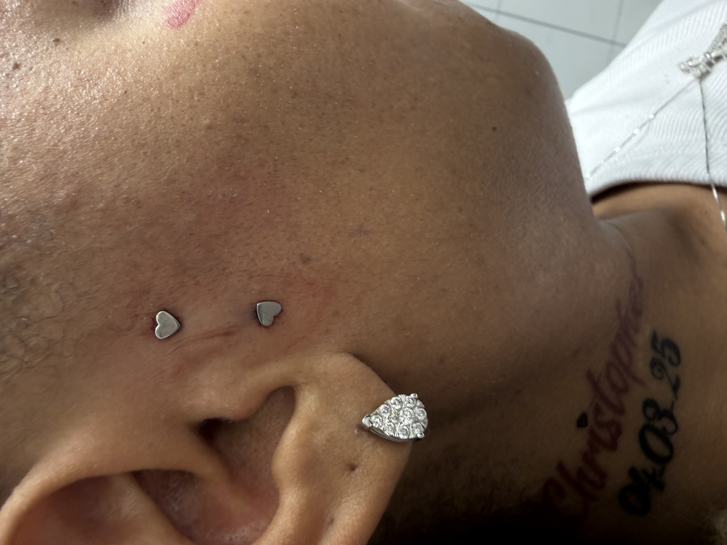 Close-up of a person's face showing skin texture, earrings, and tattoos, with visible nose and mouth area.