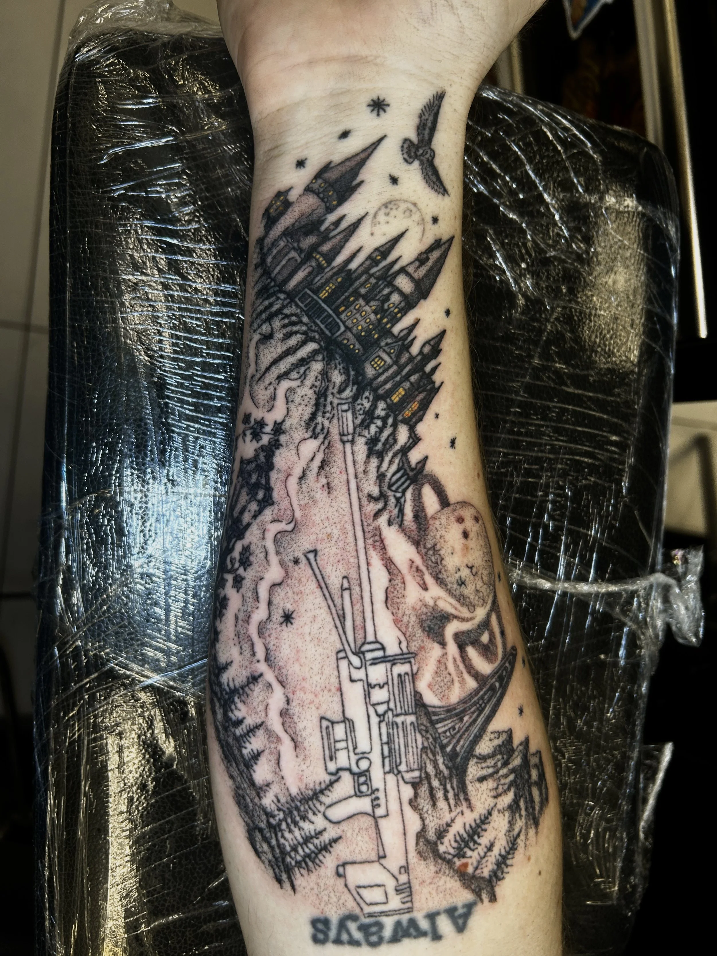 Black line tattoo on person's forearm depicting a train moving through a mountainous landscape with falling snow, a full moon, and stars in the sky.