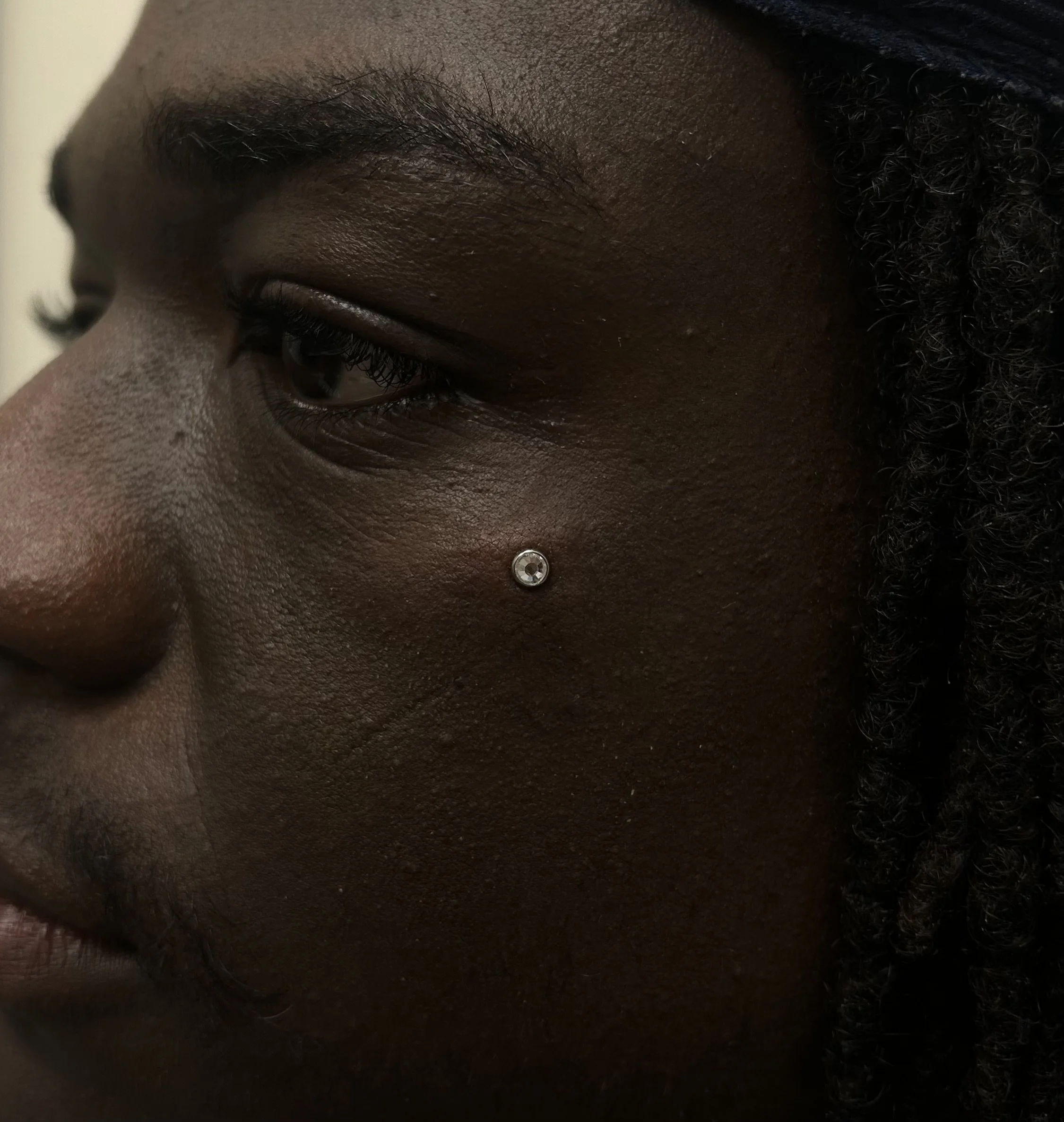 Close-up of a person's face showing one eye, ear, and part of the nose, with visible hair and a nose piercing.