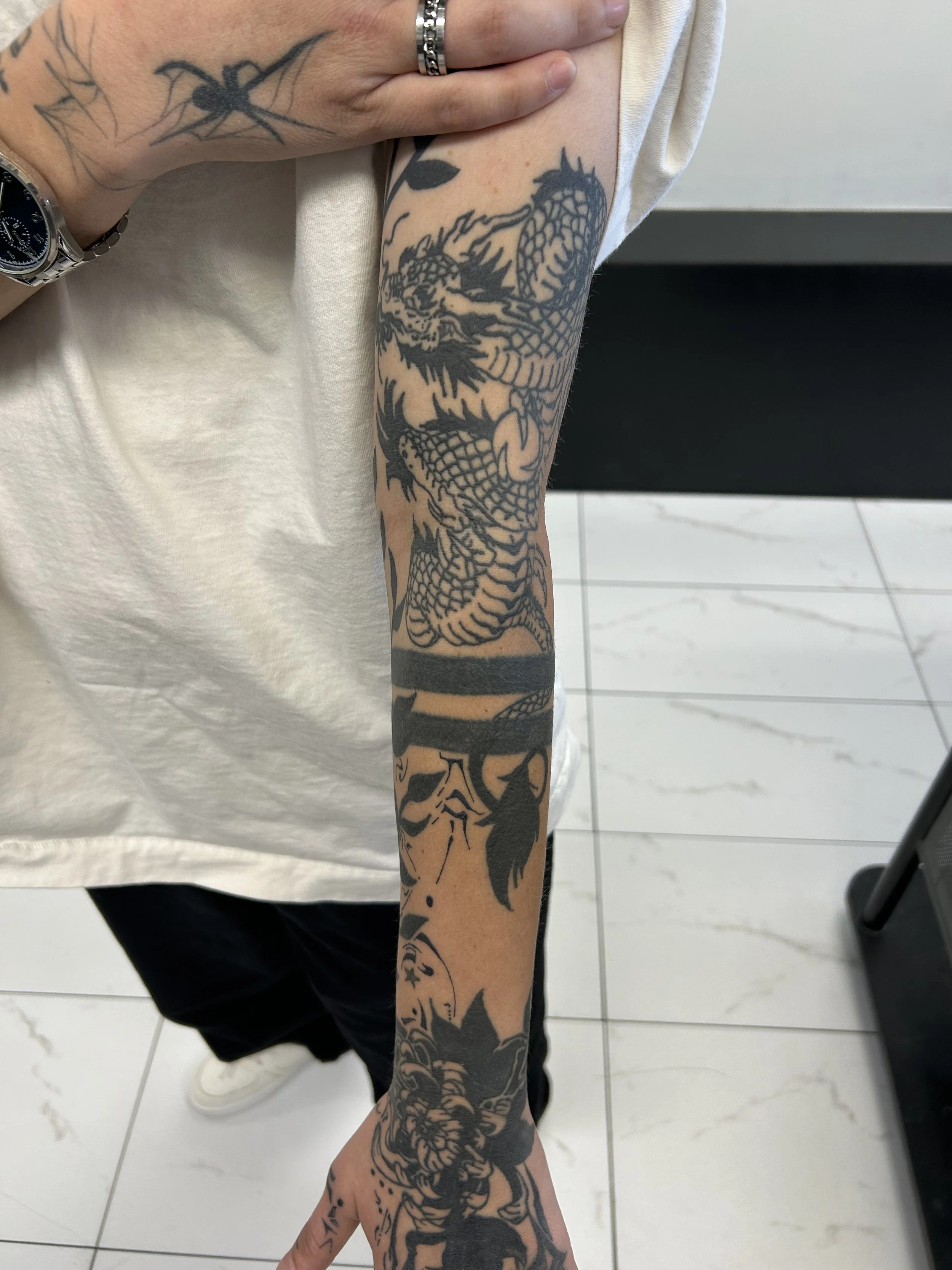Black tattoo sleeve featuring a dragon on a person's arm.