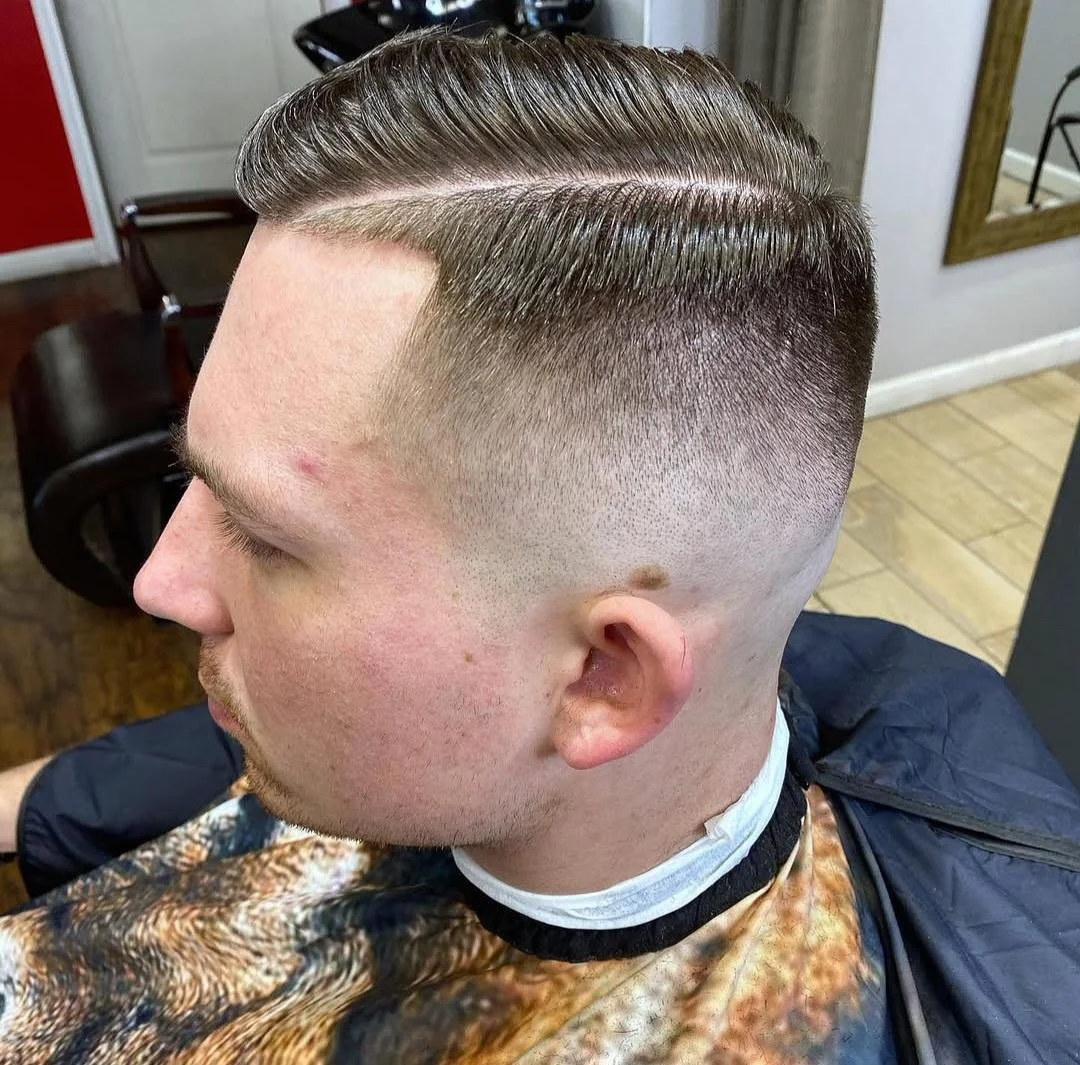 Man with a classic high fade haircut and slicked-back hair, sitting in a barbershop chair.