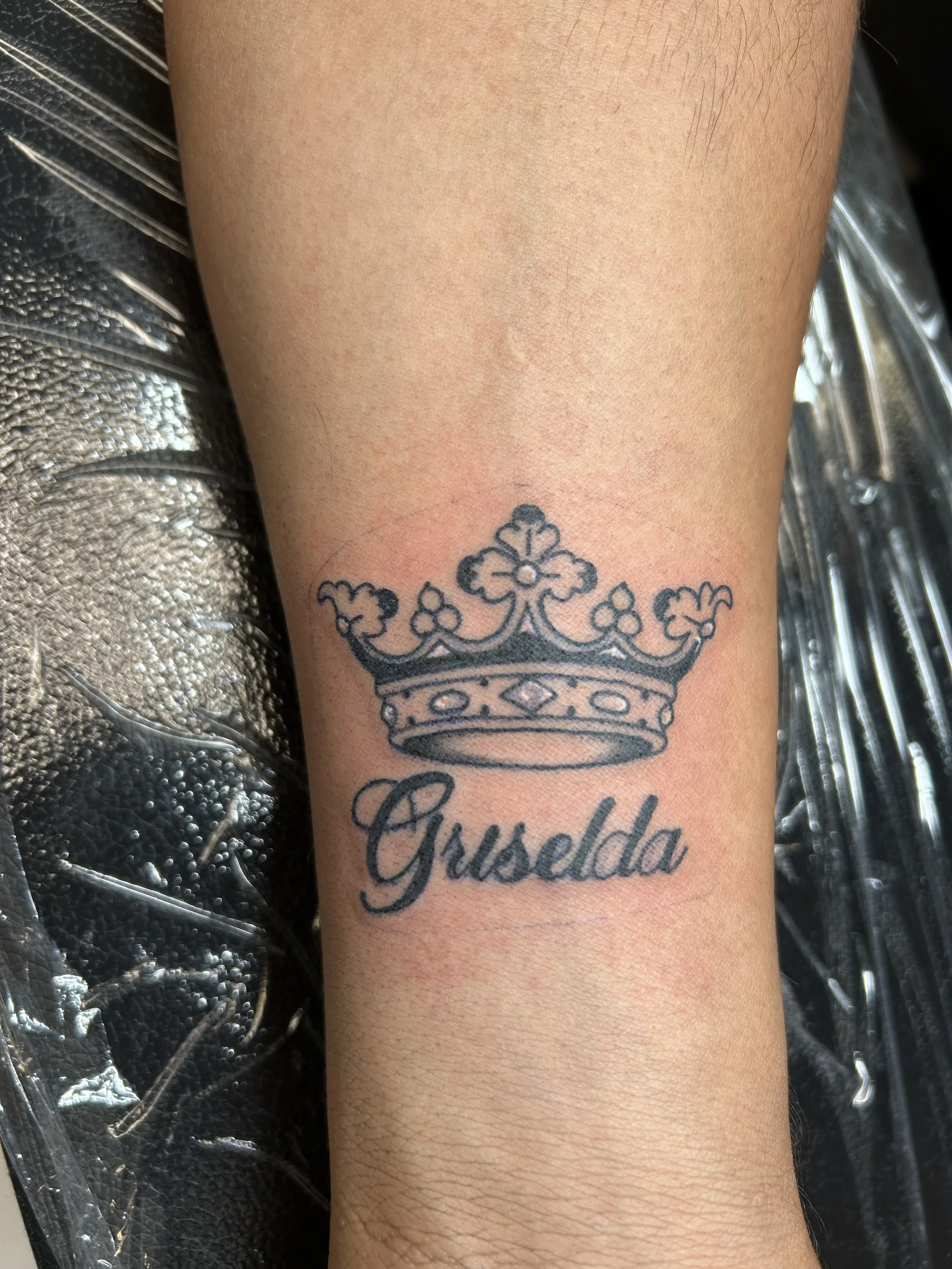 Tattoo of a crown with the name 'Gusselda' written underneath on a person's forearm.