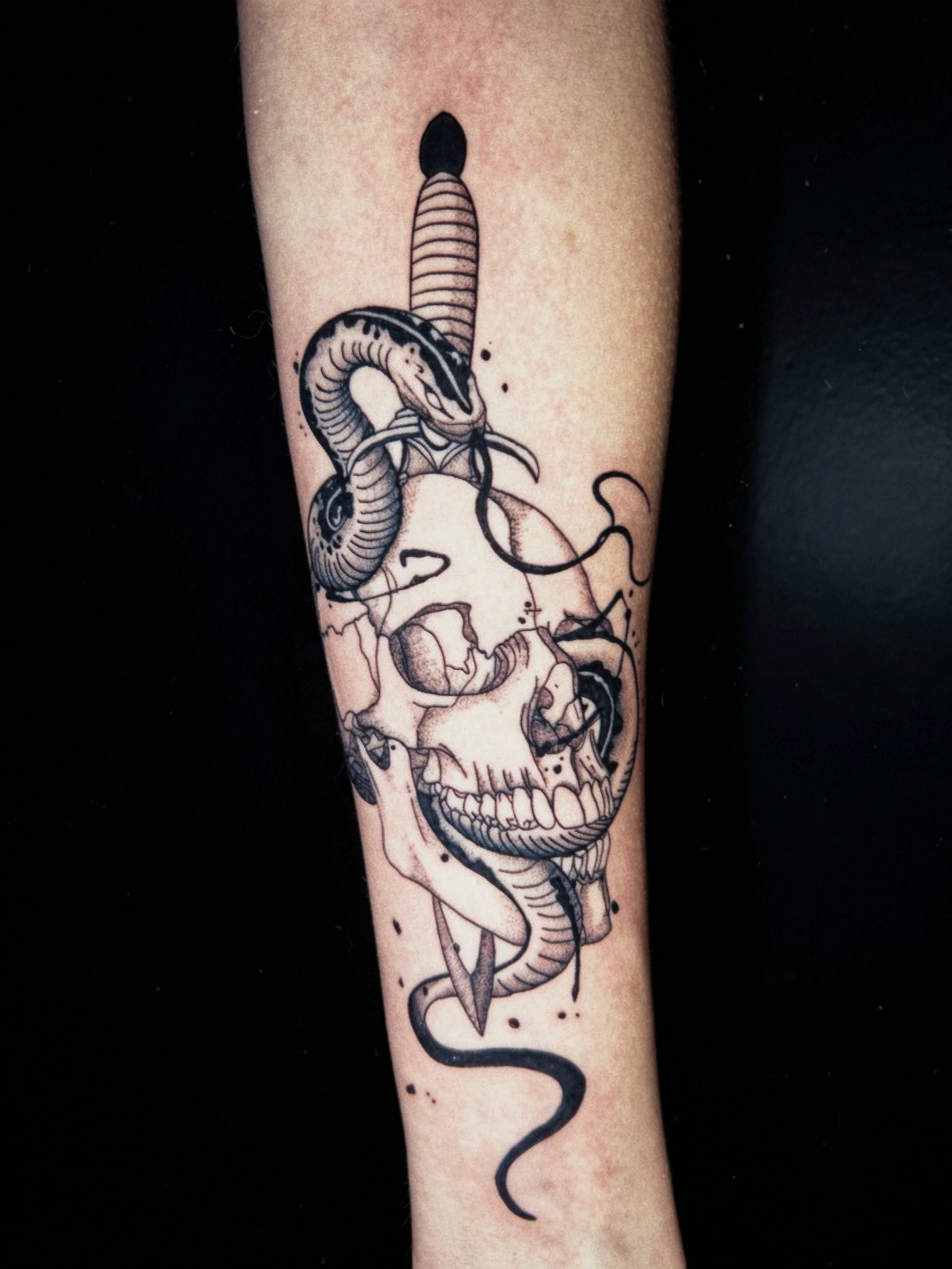 Black ink tattoo of a snake intertwined with a human skull on a person's arm.