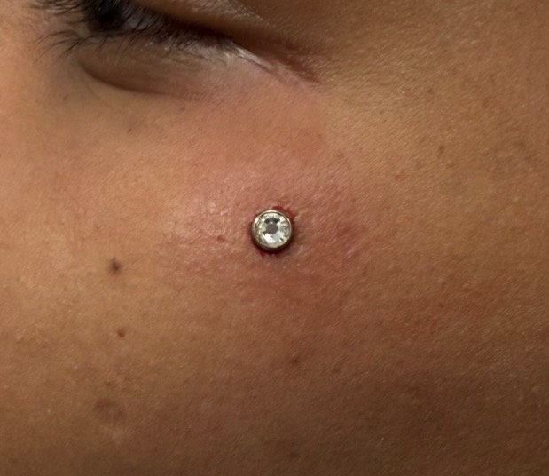 Close-up of a person's cheek with a small, clear gemstone stud piercing.