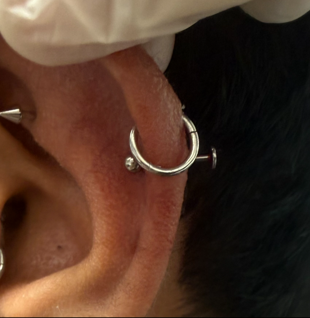 Close-up of a person's ear with a silver hoop earring and black hair.