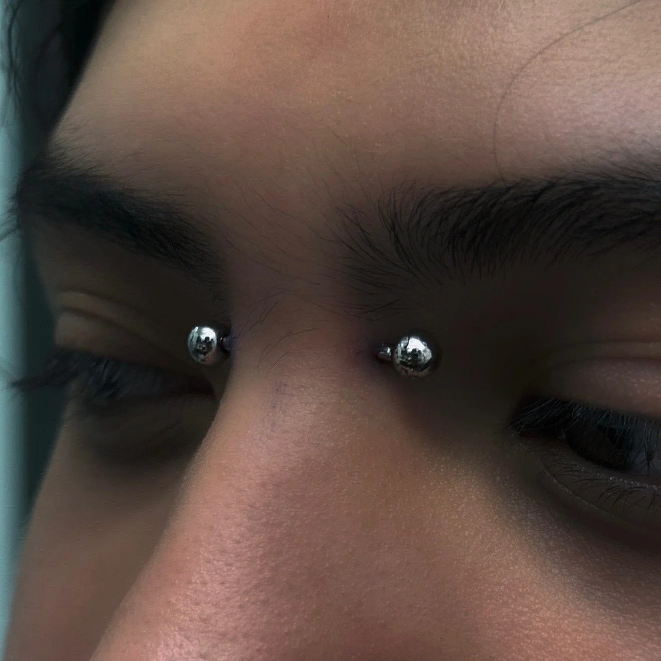 Close-up of a person's face with metal piercings in the eyebrows and nose.