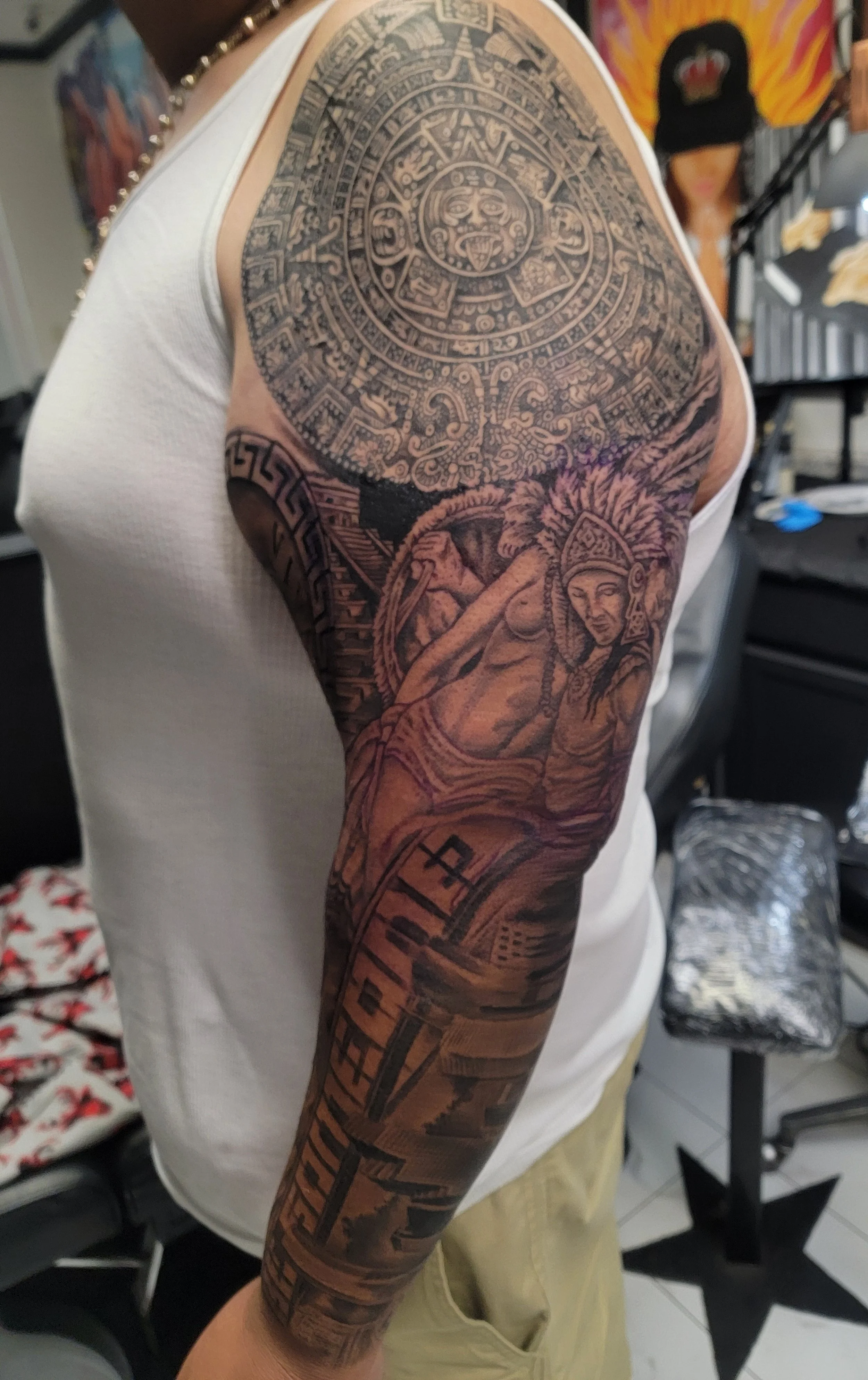 Tattoo sleeve featuring Aztec calendar and an indigenous woman wearing traditional attire with feathered headdress.