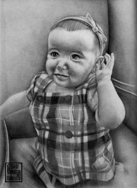 Black and white photo of a baby girl with a headband and plaid dress, smiling and holding her hand to her ear.
