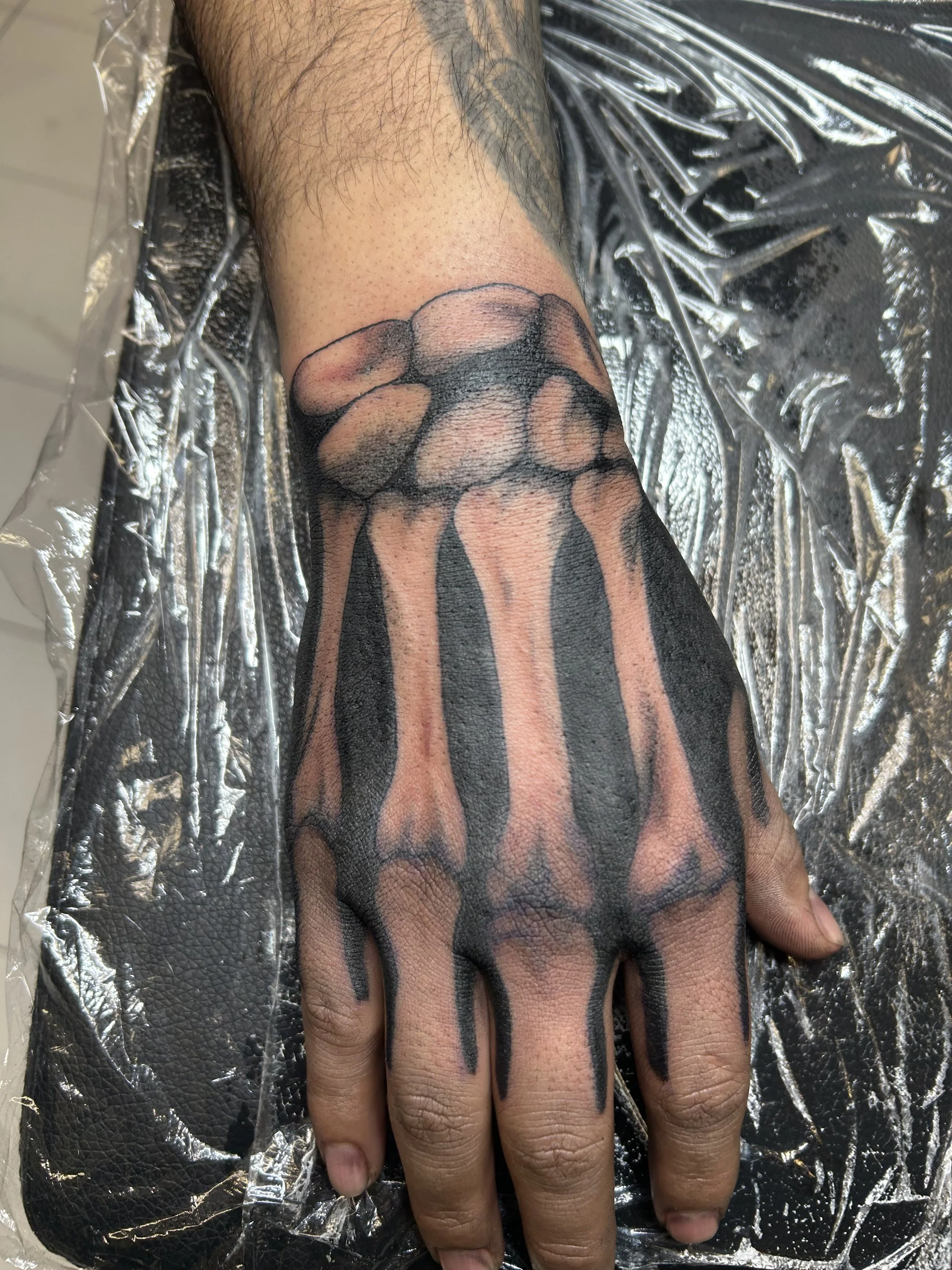 A freshly inked tattoo of skeletal fingers on a person's hand, with the bones depicted in black and shading for depth.