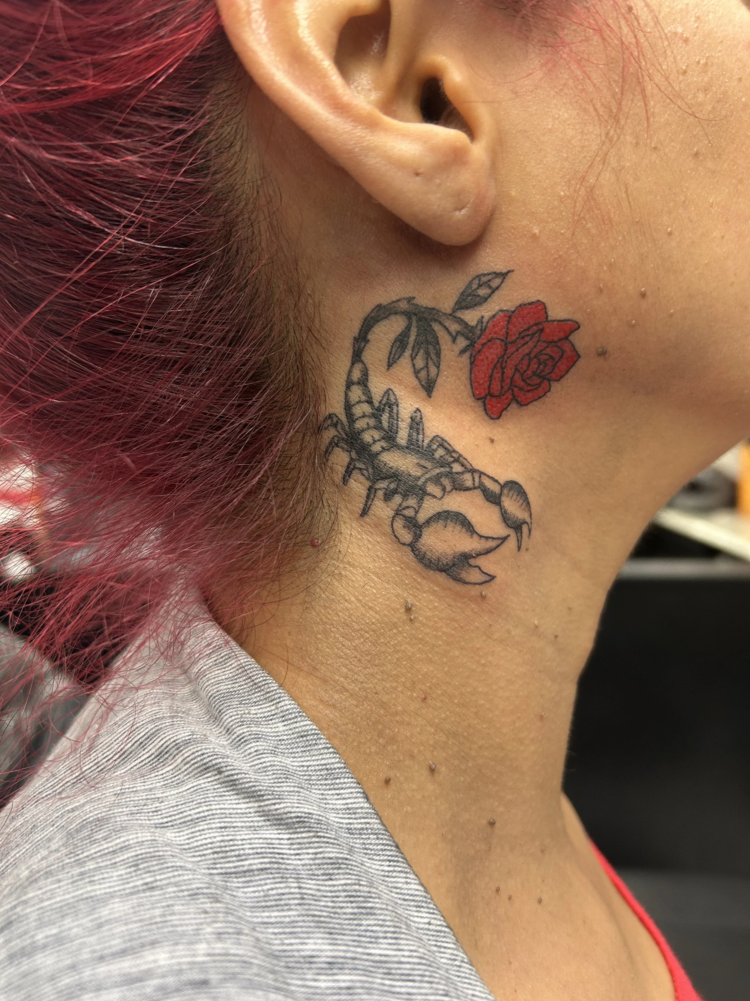 Tattoo of a black and gray scorpion with a red rose above it on the person's neck.