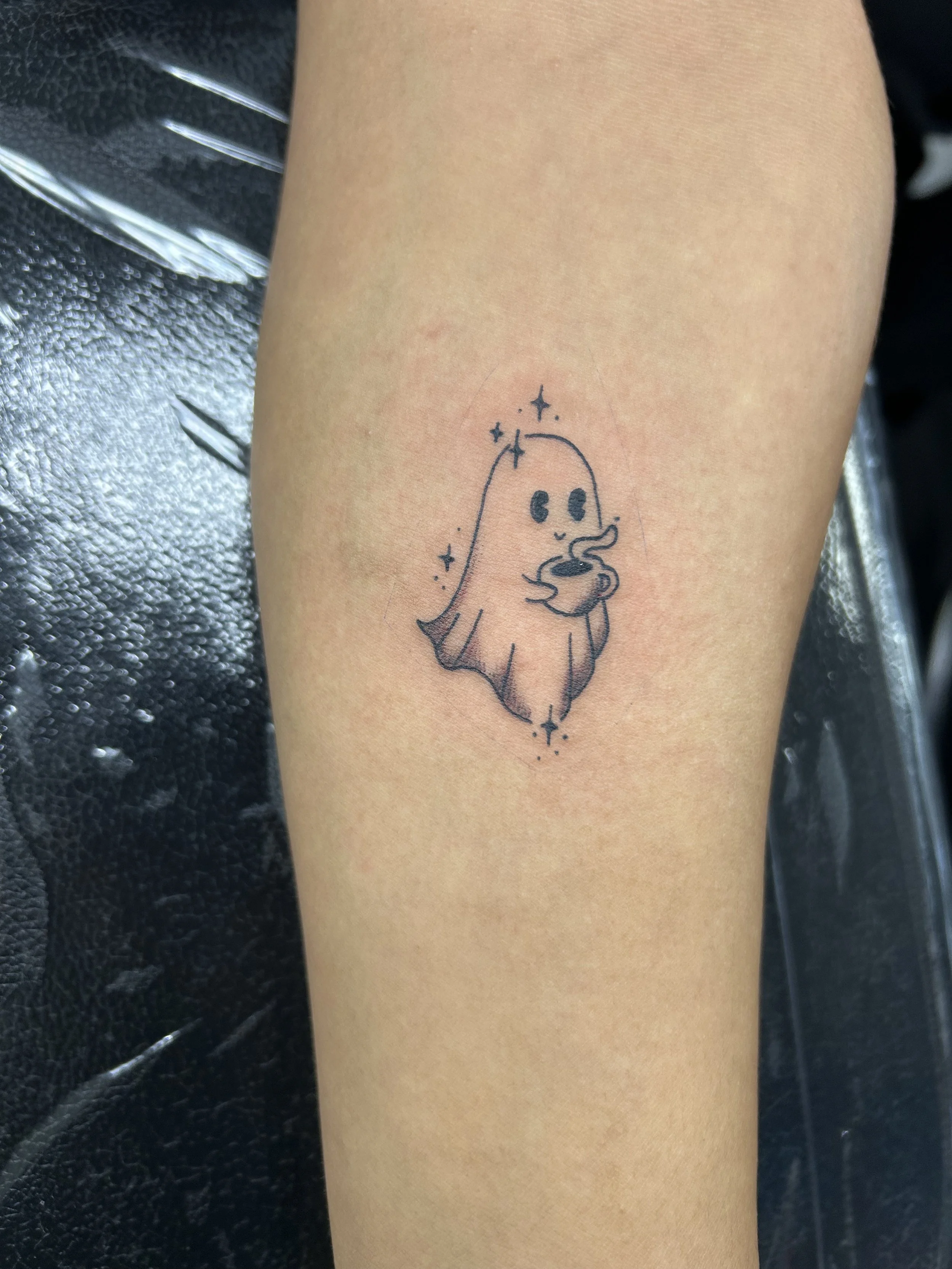 Tattoo of a ghost with big eyes and a mustache surrounded by small stars on someone's arm.