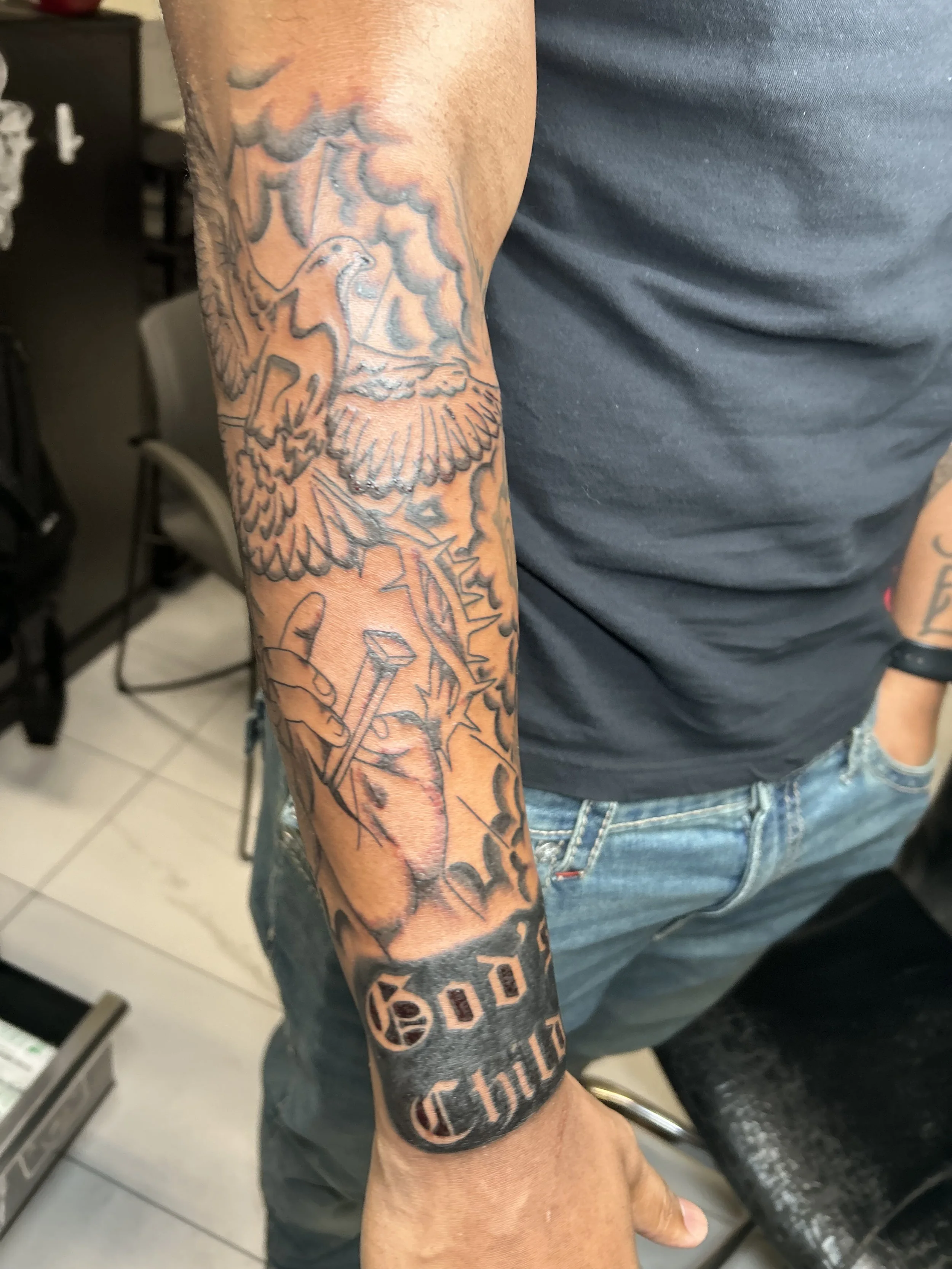 Tattoo of a phoenix rising from flames and a dagger on a person's forearm, with the word 'God' and 'Chino' in bold letters on the wrist.