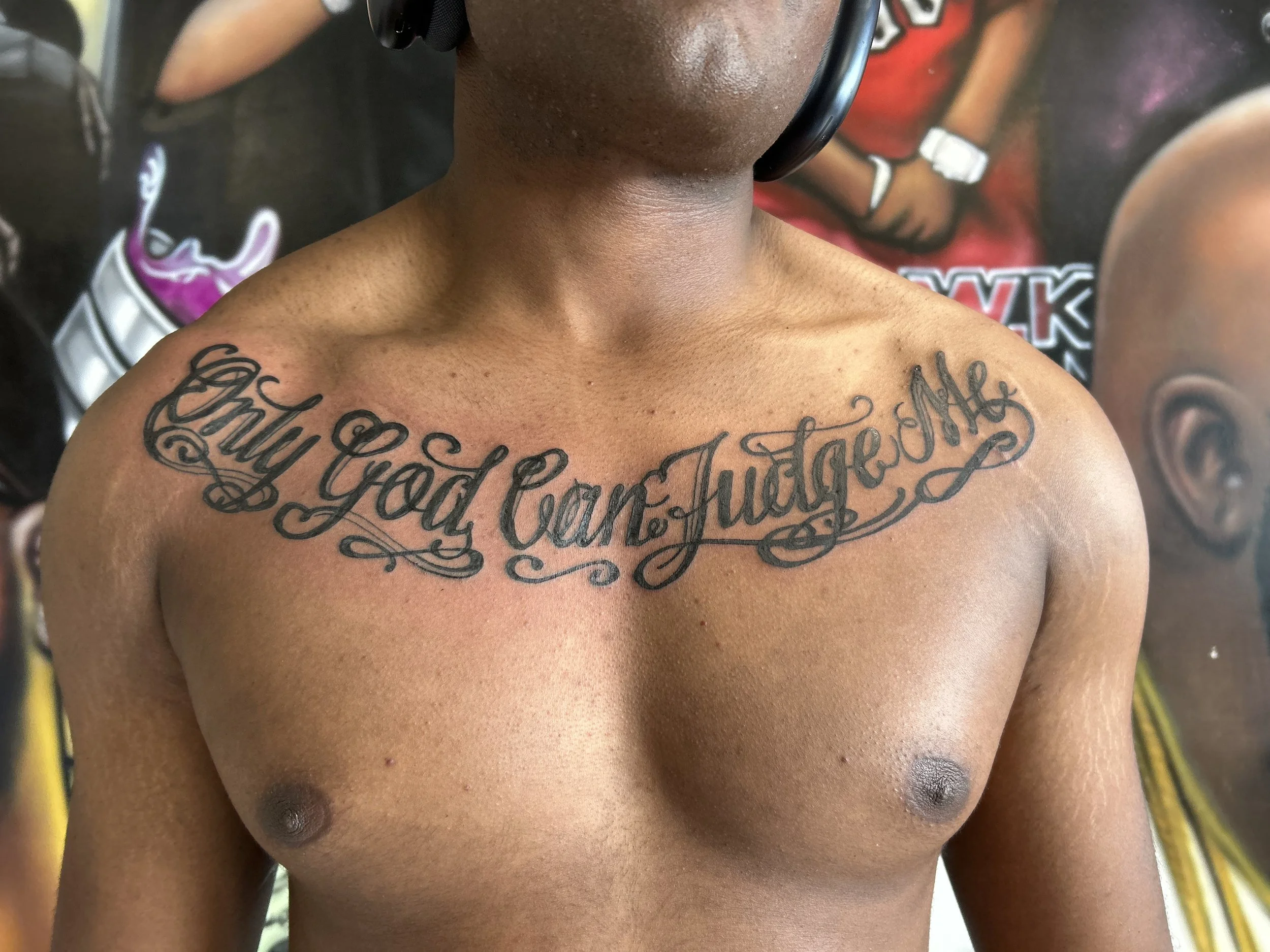 A shirtless person with a large tattoo across their chest that reads 'Only God Can Judge Me' in decorative cursive script with flourishes.
