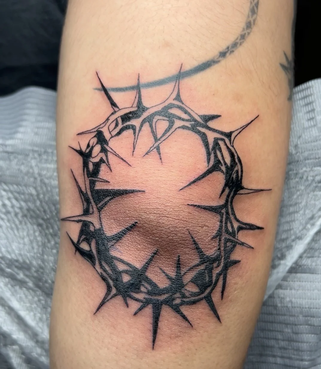 Black and gray tattoo of a crown of thorns on a person's arm.