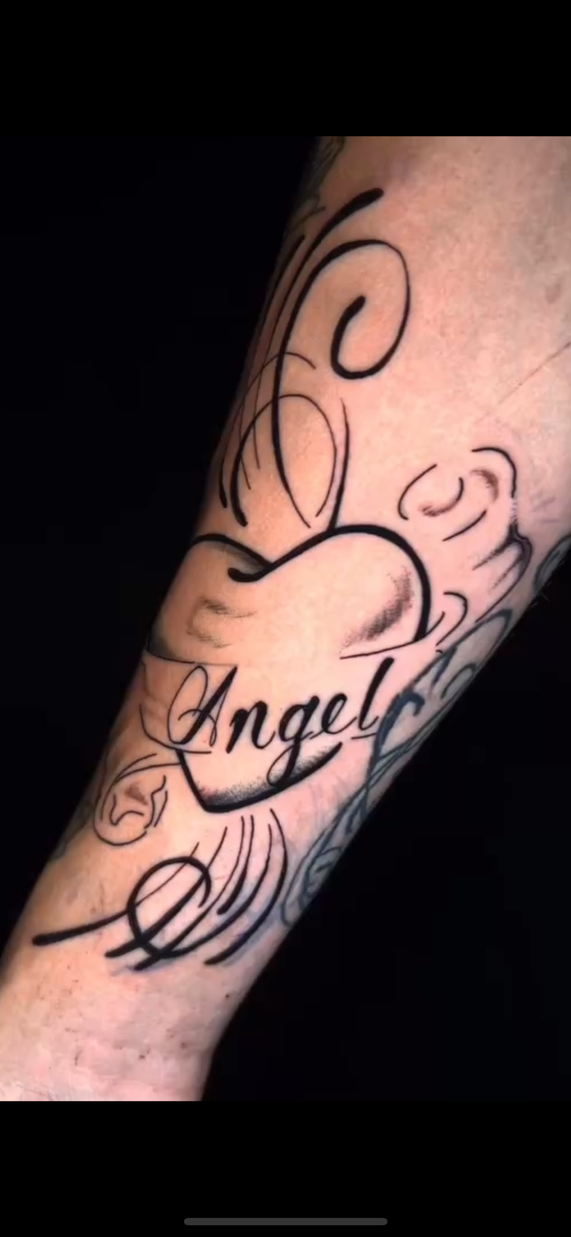 Tattoo of a cartoon character with the word 'Angel' inside a heart on a person's arm.