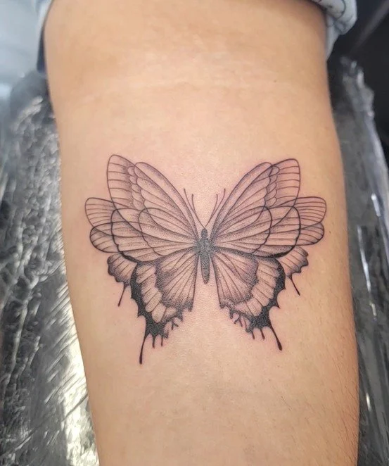 A butterfly tattoo on a person's arm with detailed line work and shading.