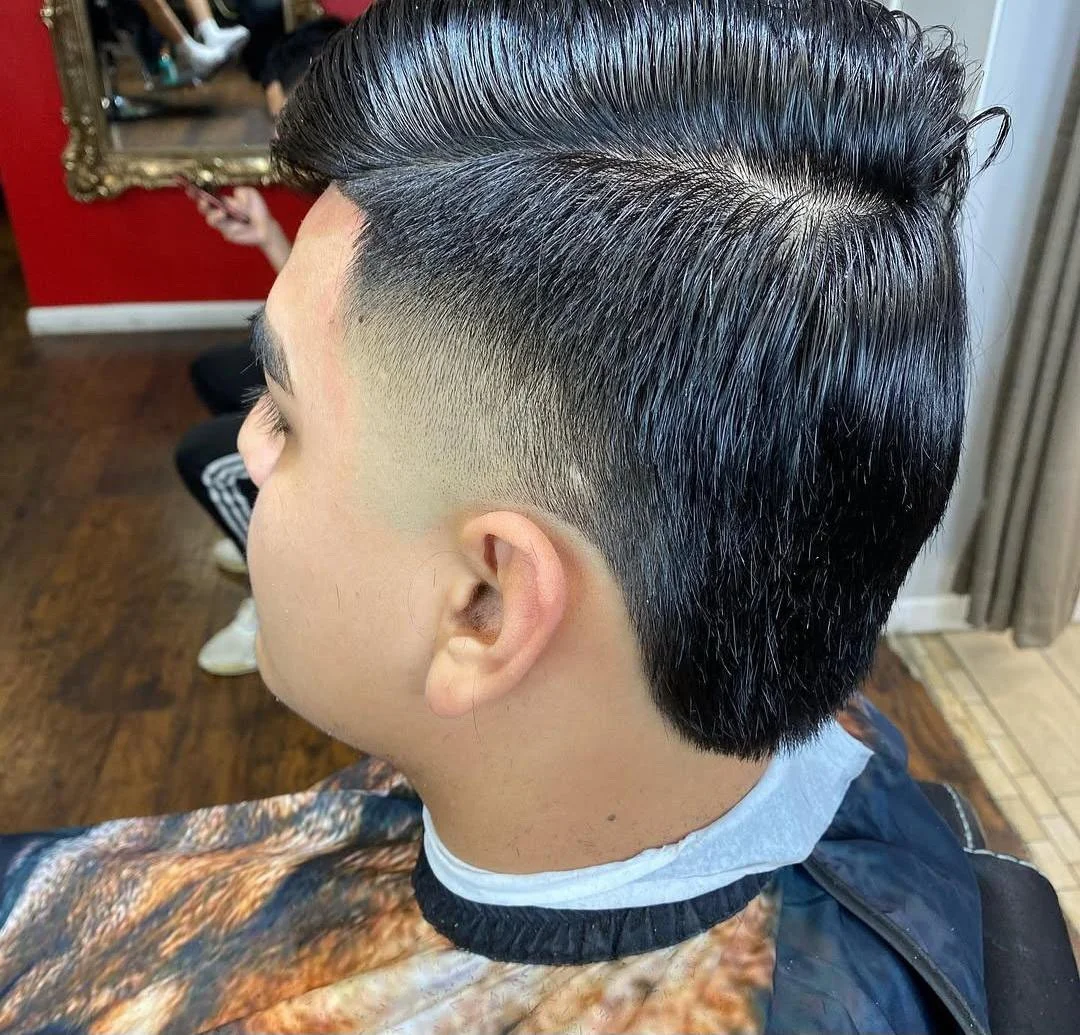 Side view of a man with a modern fade haircut, featuring a long, slicked-back top and closely shaved sides.