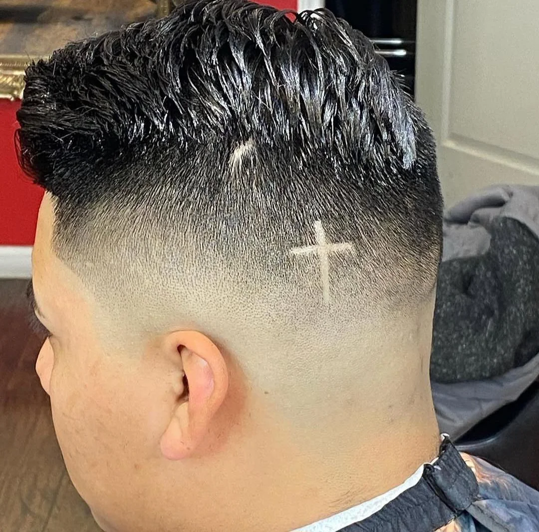 Close-up of a man's fresh hairstyle featuring a high fade with a white cross shaved into the side of his head.