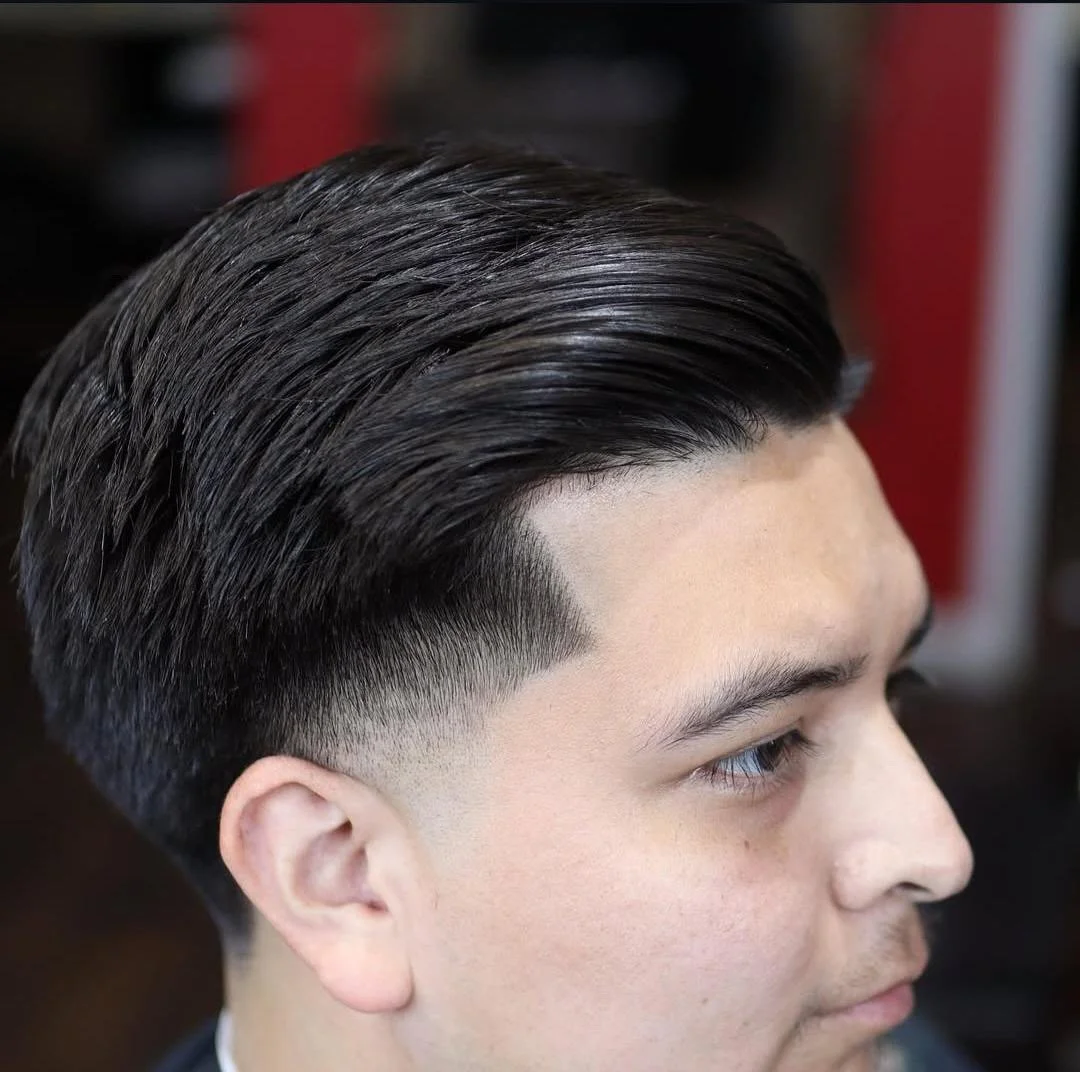 Close-up of a man's hairstyle with slicked-back dark hair and a fade on the sides.
