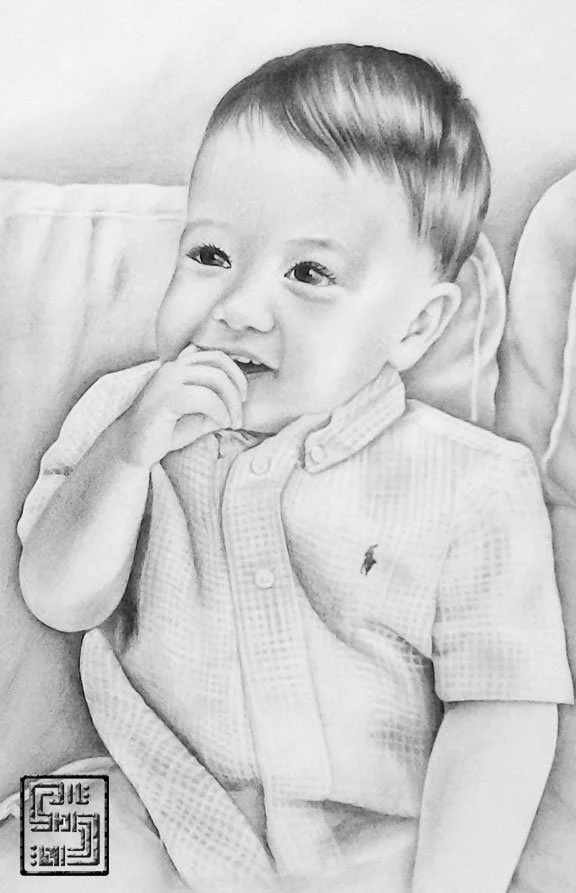 A young boy with short hair sitting on a couch, smiling and holding his fingers to his mouth, wearing a collared shirt with a small logo.