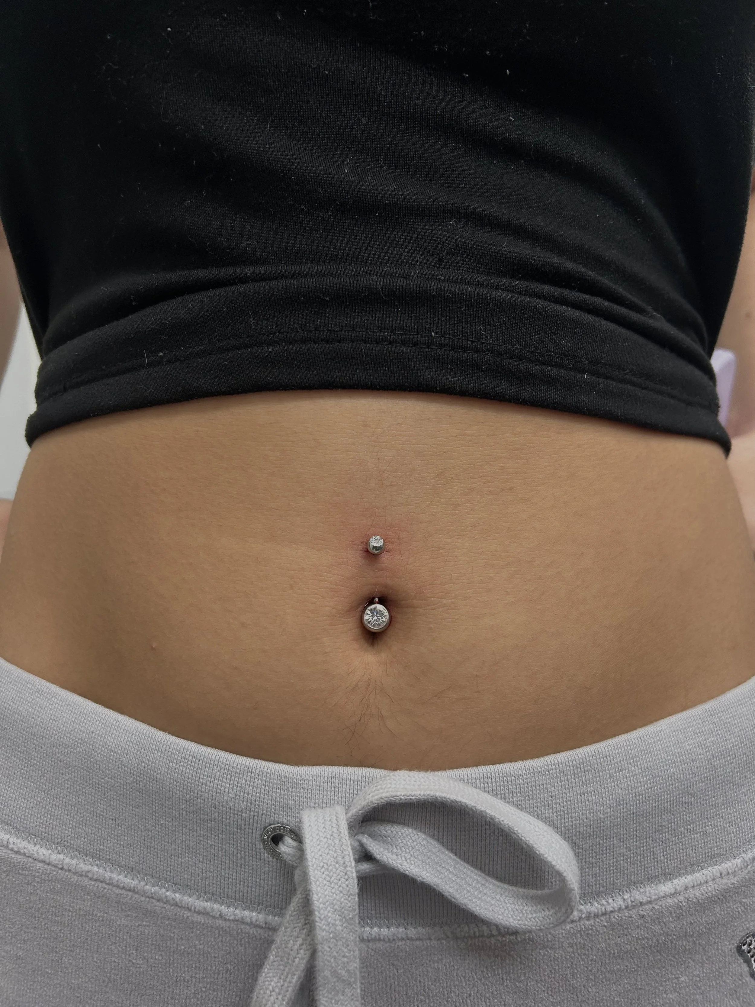 Close-up of a person's midsection with a belly button piercings and a pair of gray sweatpants with a drawstring.