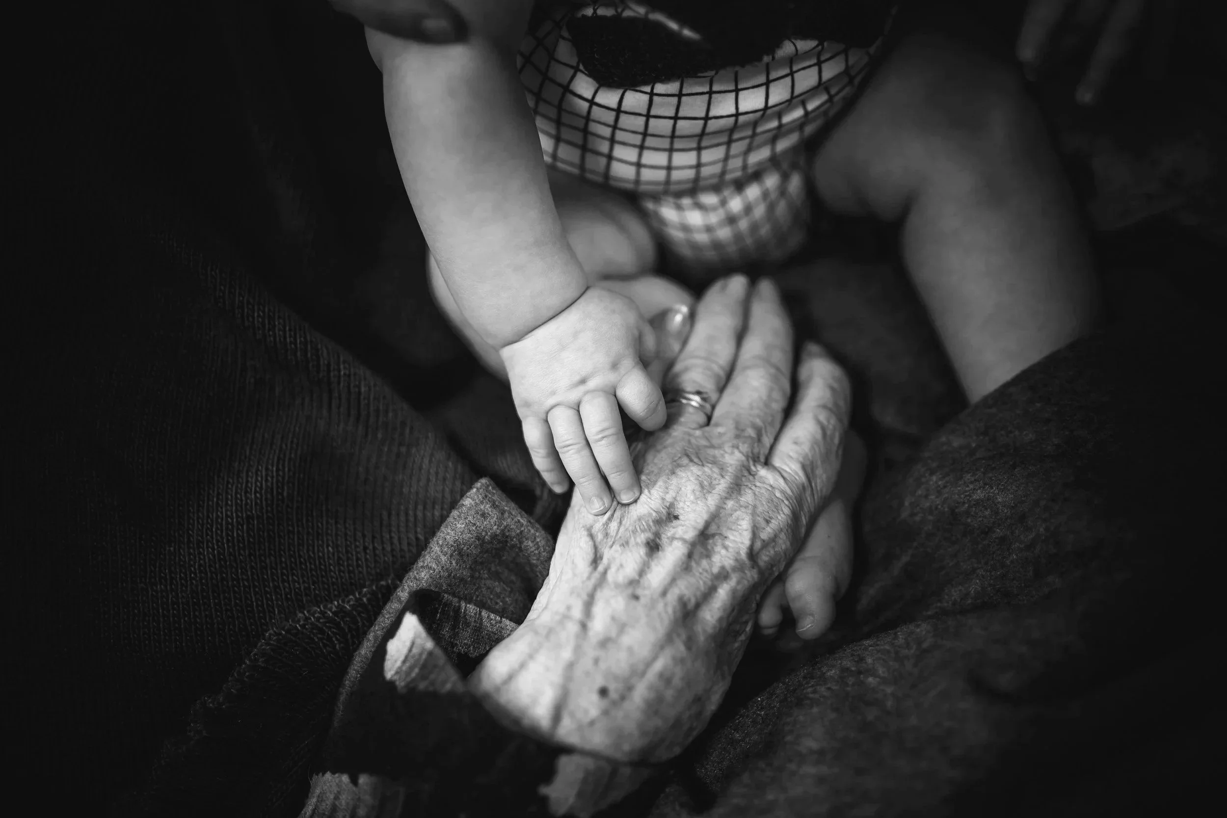 A young child's hand rests on an elderly person's hand, both hands touching gently.