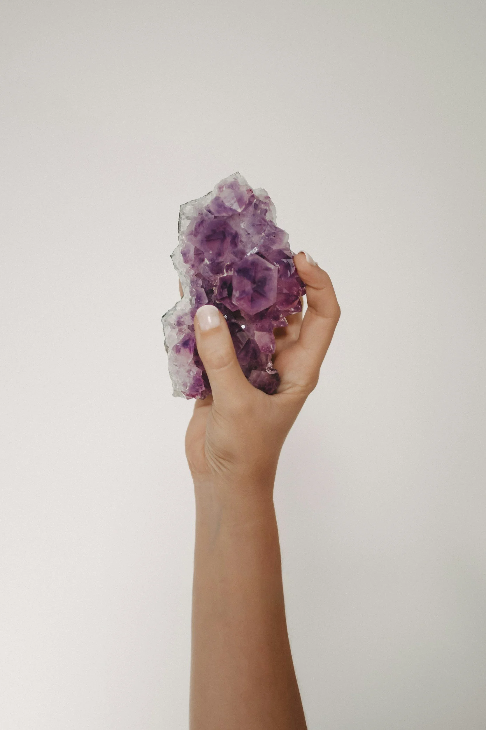 A hand holding a large, purple and clear crystal quartz gemstone against a plain white background.