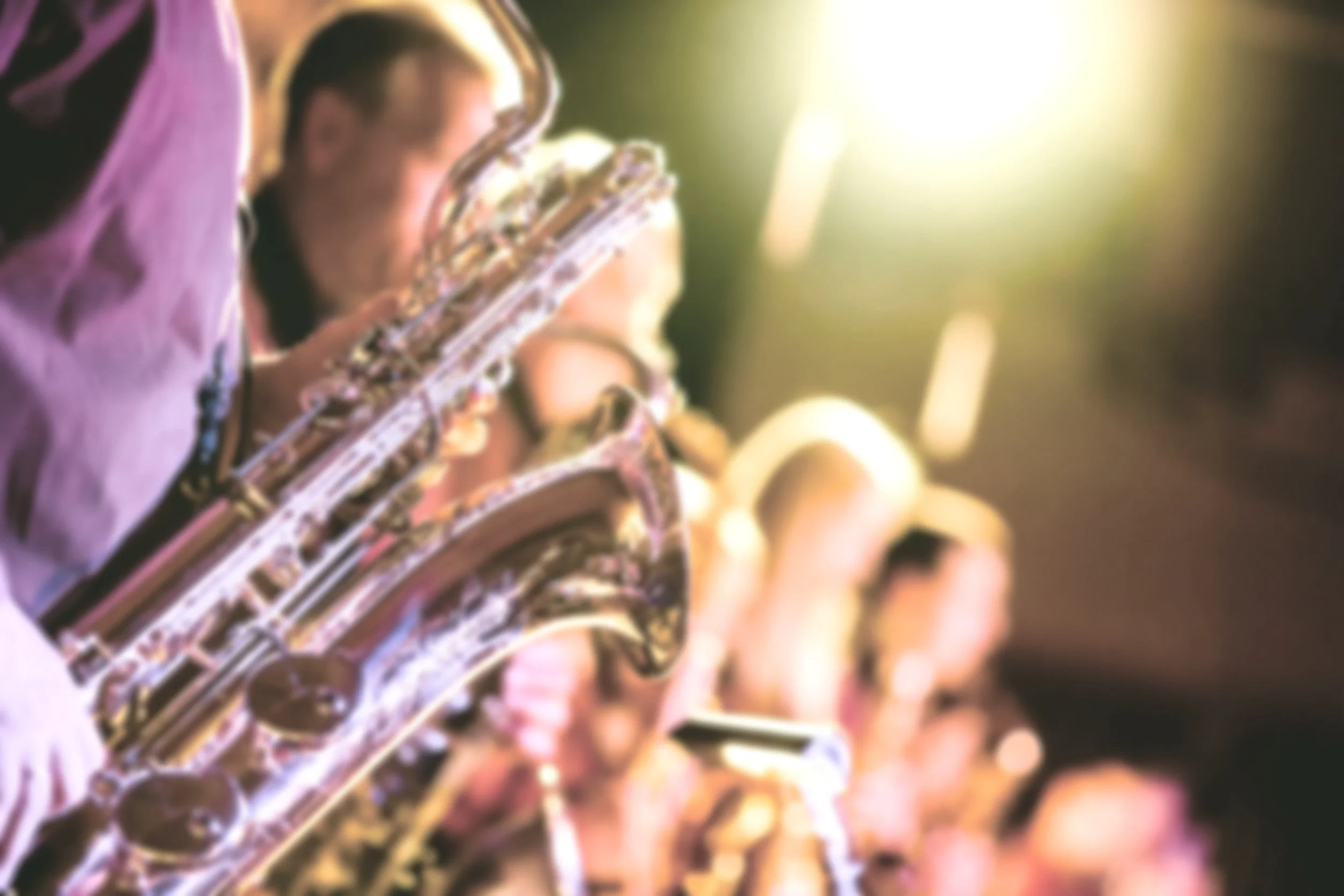 View of saxophone, sax player hands on keys with in a small jazz club in the background.