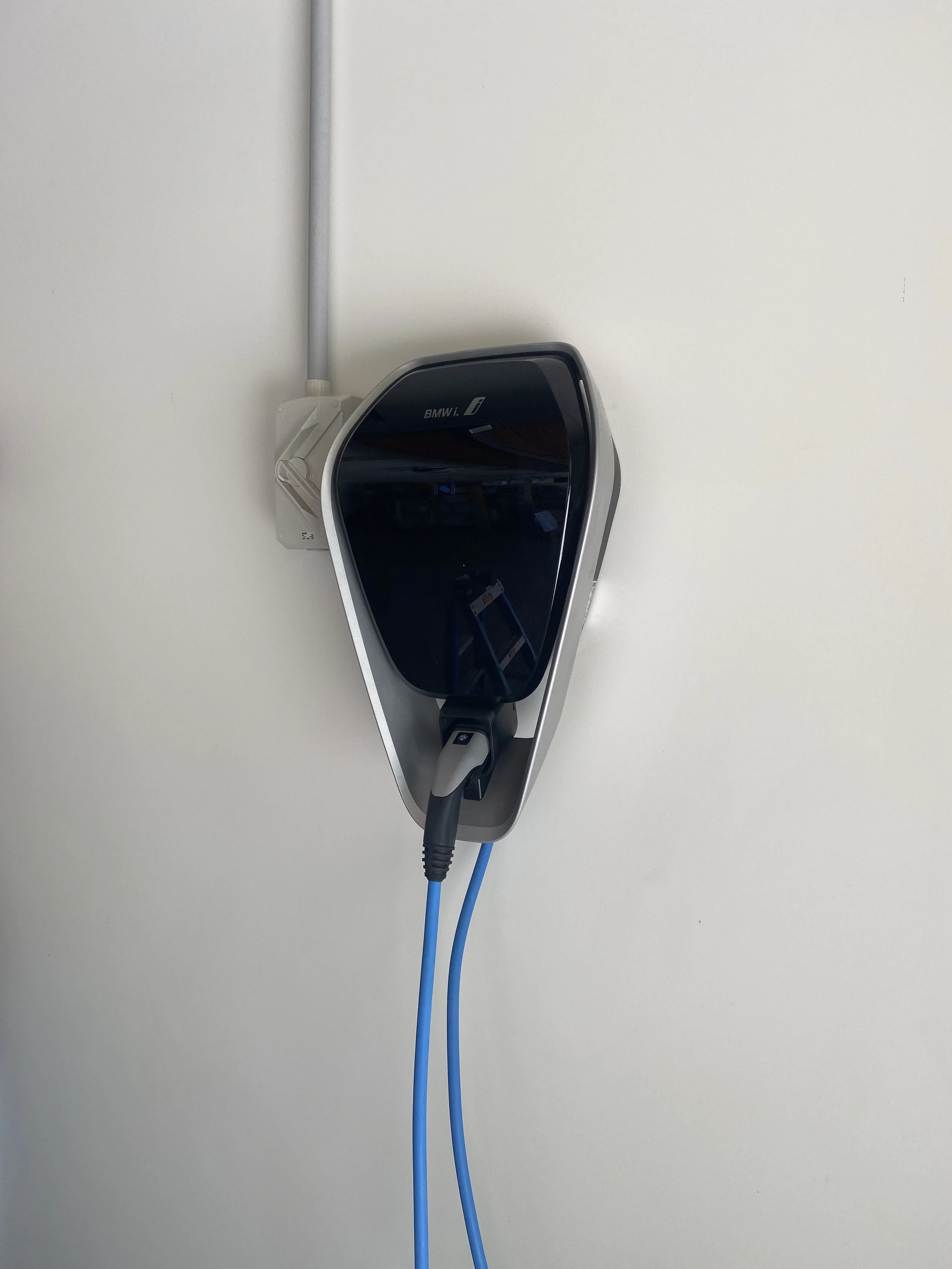 Electric vehicle charging station installed on a white wall, with two blue charging cables connected.