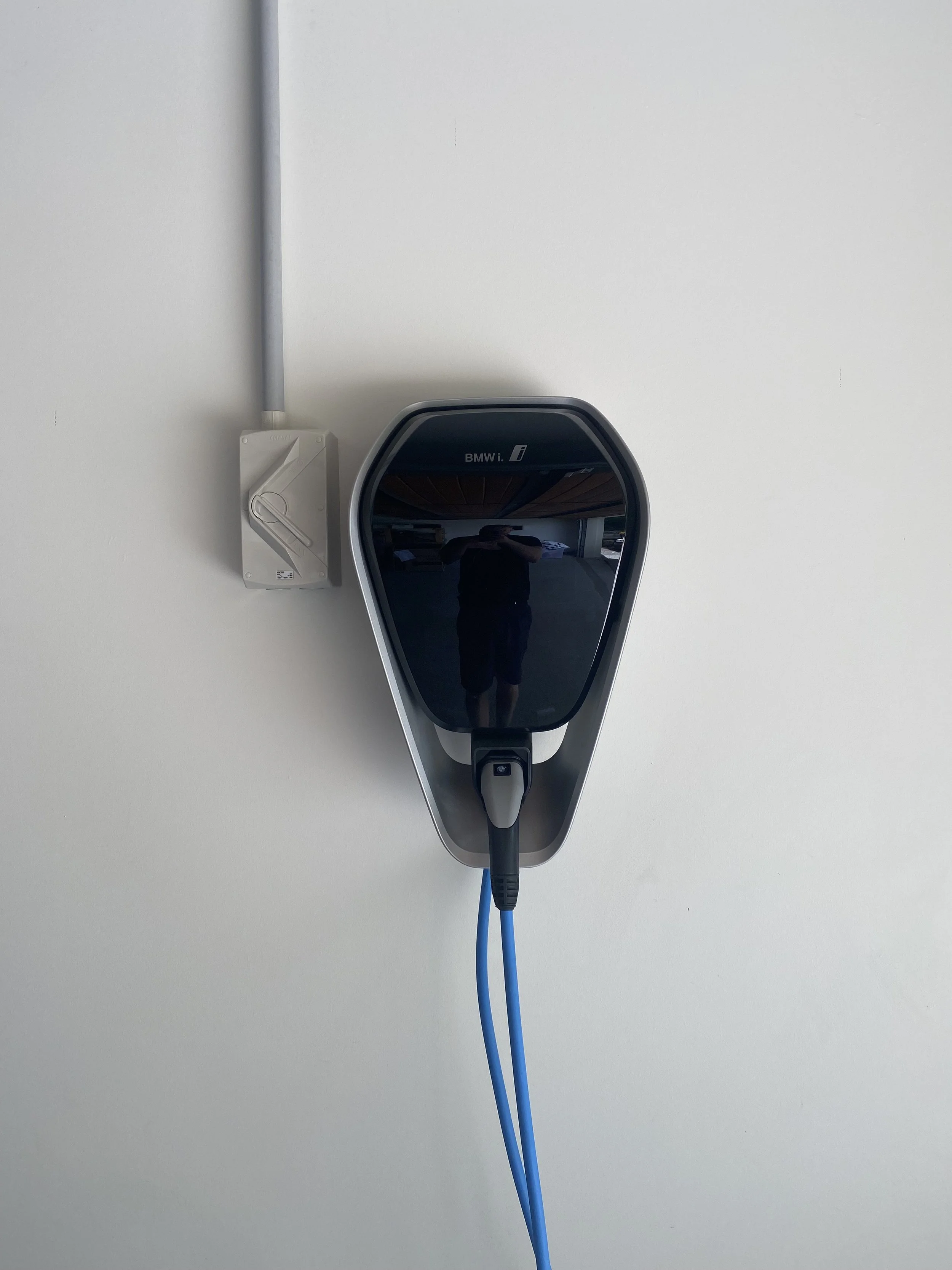 Electric vehicle charging station with a black and silver charger and blue charging cable mounted on a white wall.