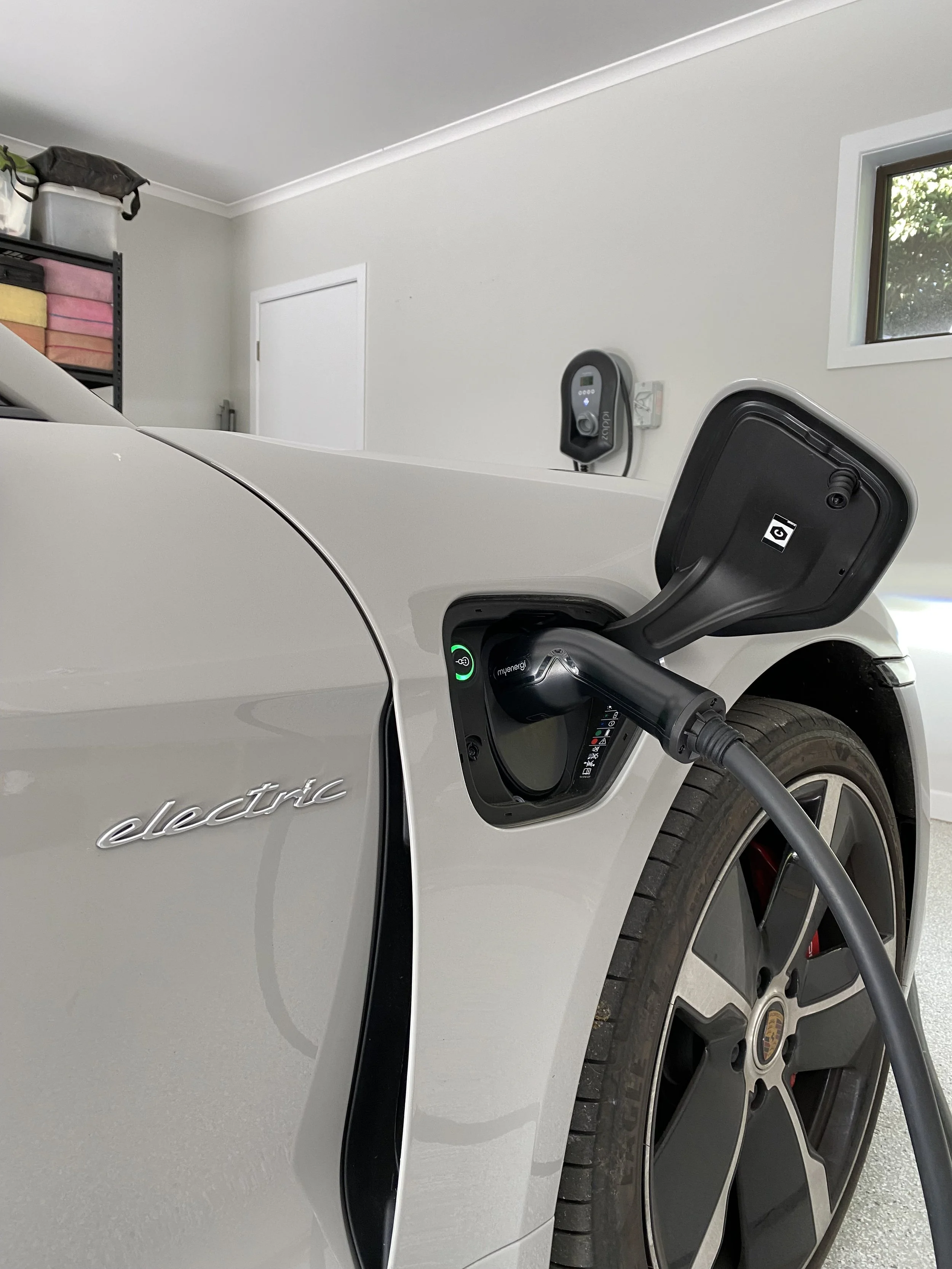 White electric car plugged into a charging station in a garage, with a sticker labeled 'electric' on the side of the car.