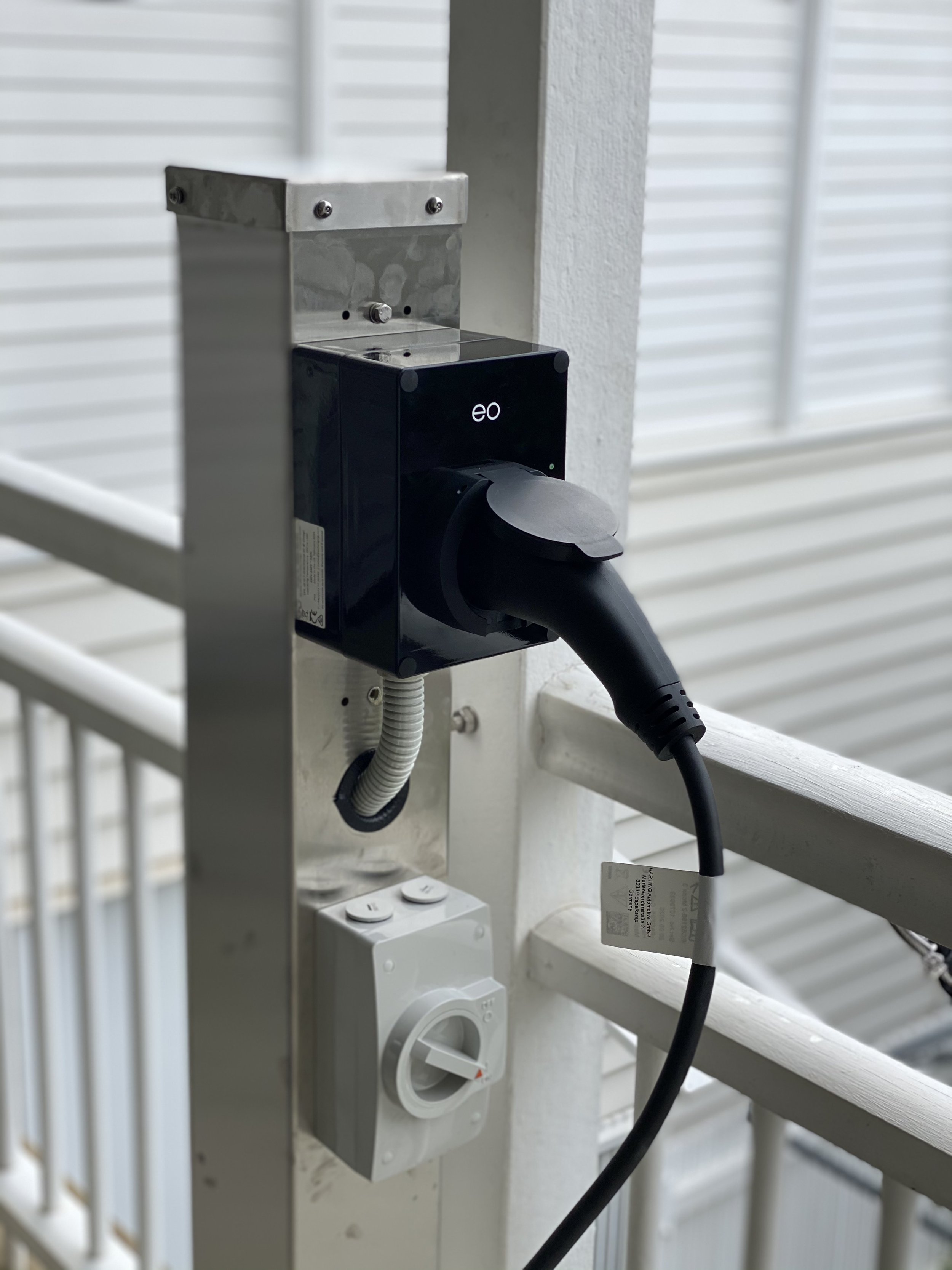 Charging station with an electric vehicle plug and a power switch on a balcony railing.