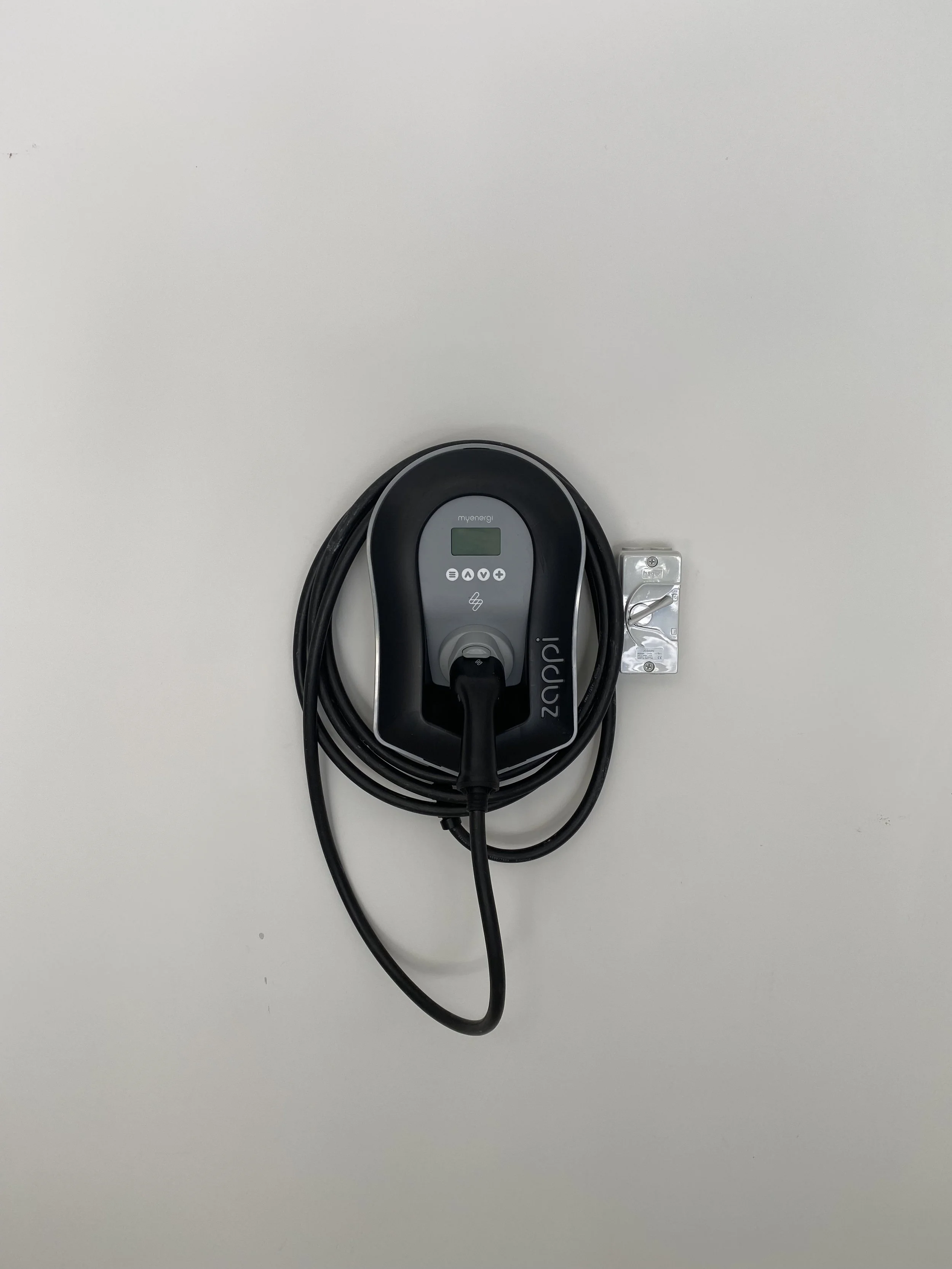 Electric vehicle charging station mounted on a white wall with a plugged-in cable.