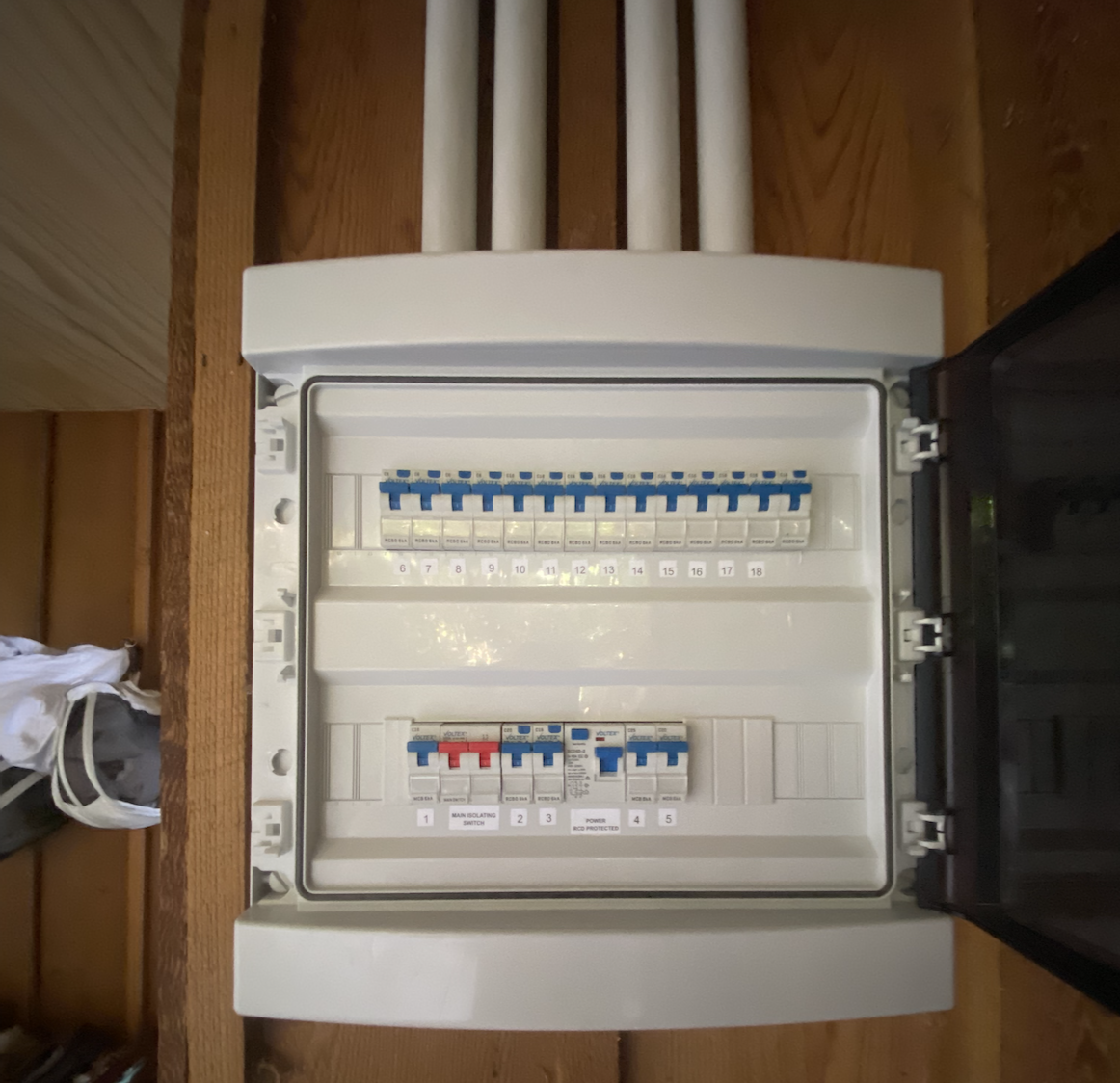 Open electrical panel containing circuit breakers on a wooden wall.