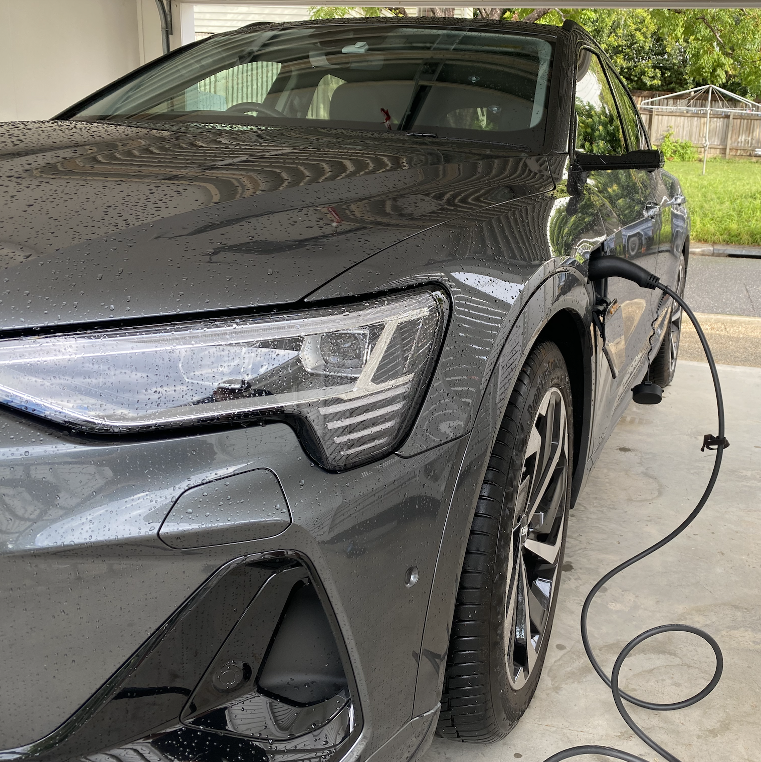 A gray electric car parked in a garage charging with a charging cable connected to the front side.