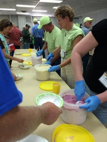 People in green shirts and blue gloves preparing or serving food at a community event or food distribution.