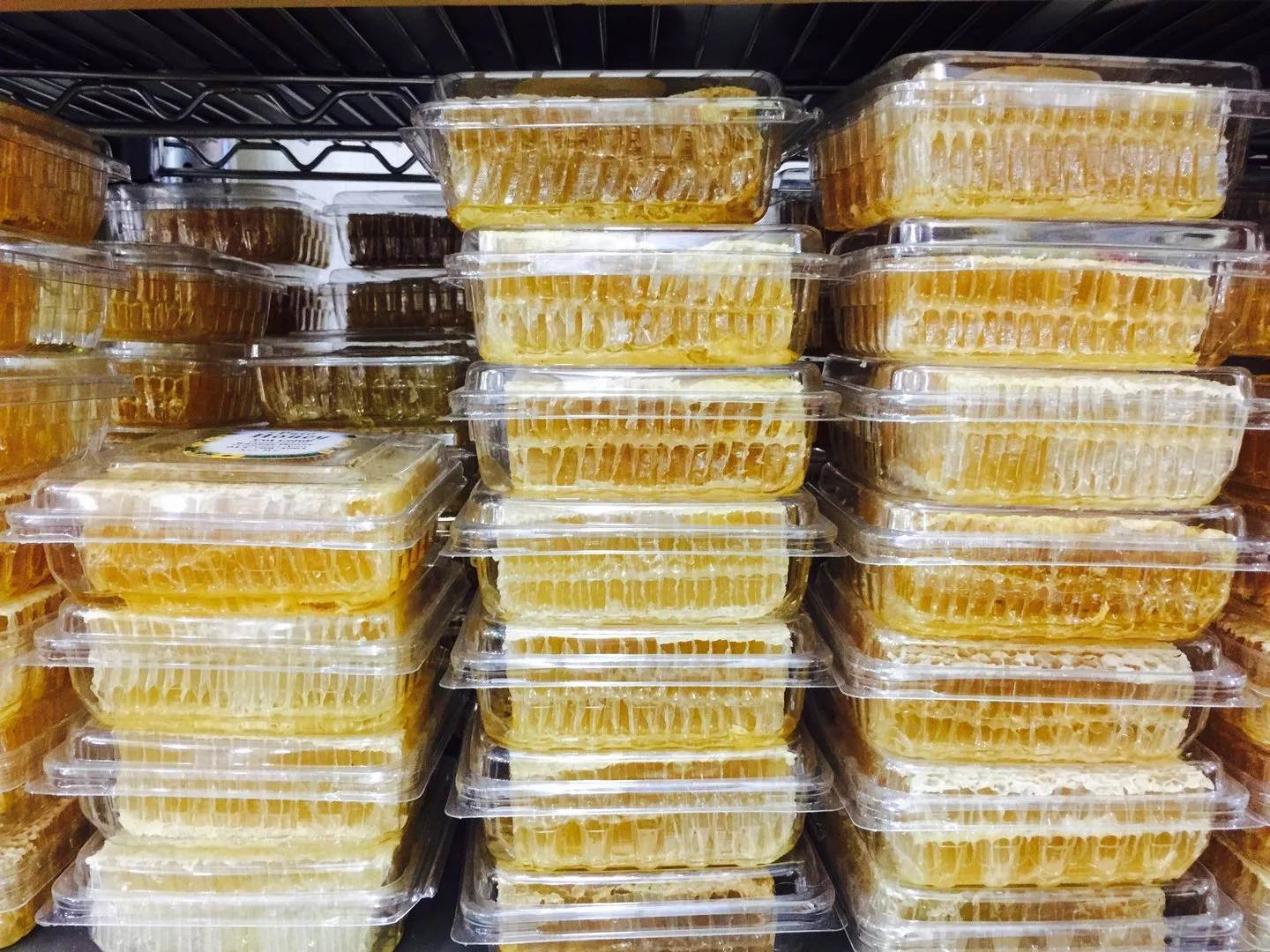 Stacked rectangular containers of honey on a metal shelf.