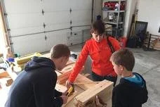 Three people working on a woodworking project in a garage.