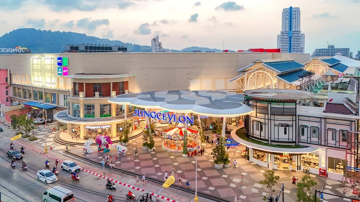 A shopping mall named JUNG Ceylon with children’s rides and tourists in front, multi-story buildings in the background, and a busy street with cars and motorcycles in the foreground.