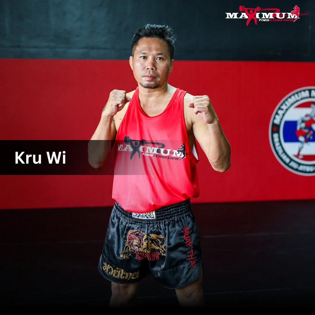 A man in a red Muay Thai training uniform posing with fists raised in a fighting stance inside a martial arts gym. The background shows a red and black wall with a logo and text for a fitness and combat center.