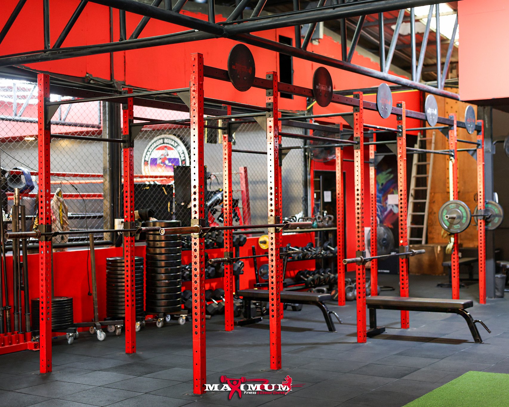 Red and black gym equipment, including weight racks, barbells, and weight plates in a gym with a black rubber floor.