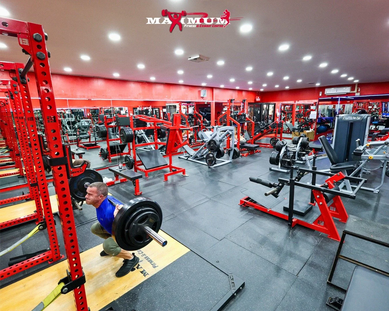 A man lifting weights with a barbell in a well-lit gym filled with various fitness equipment.