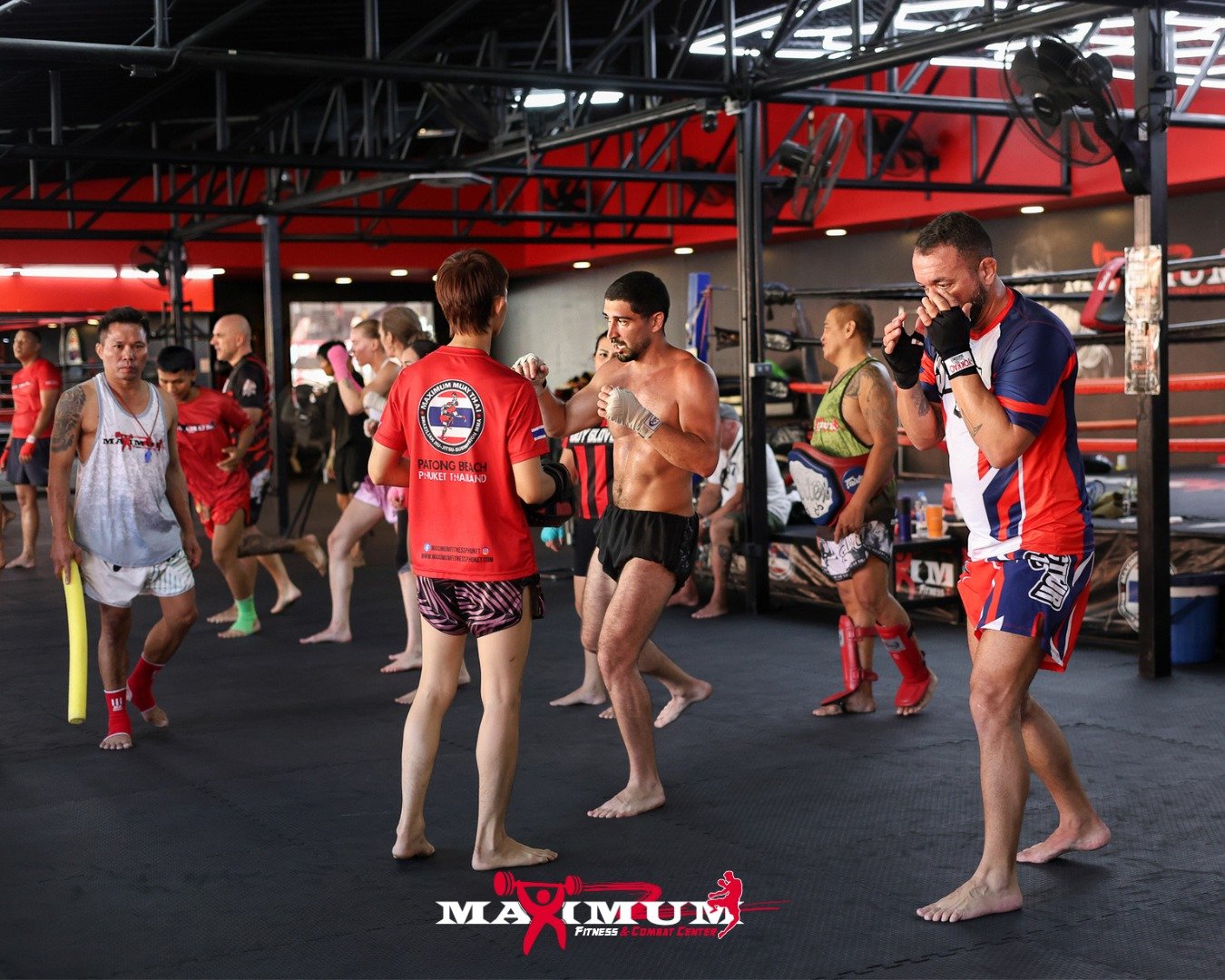 Muay Thai fighters and trainers practicing and preparing in a gym with some individuals stretching and warming up.
