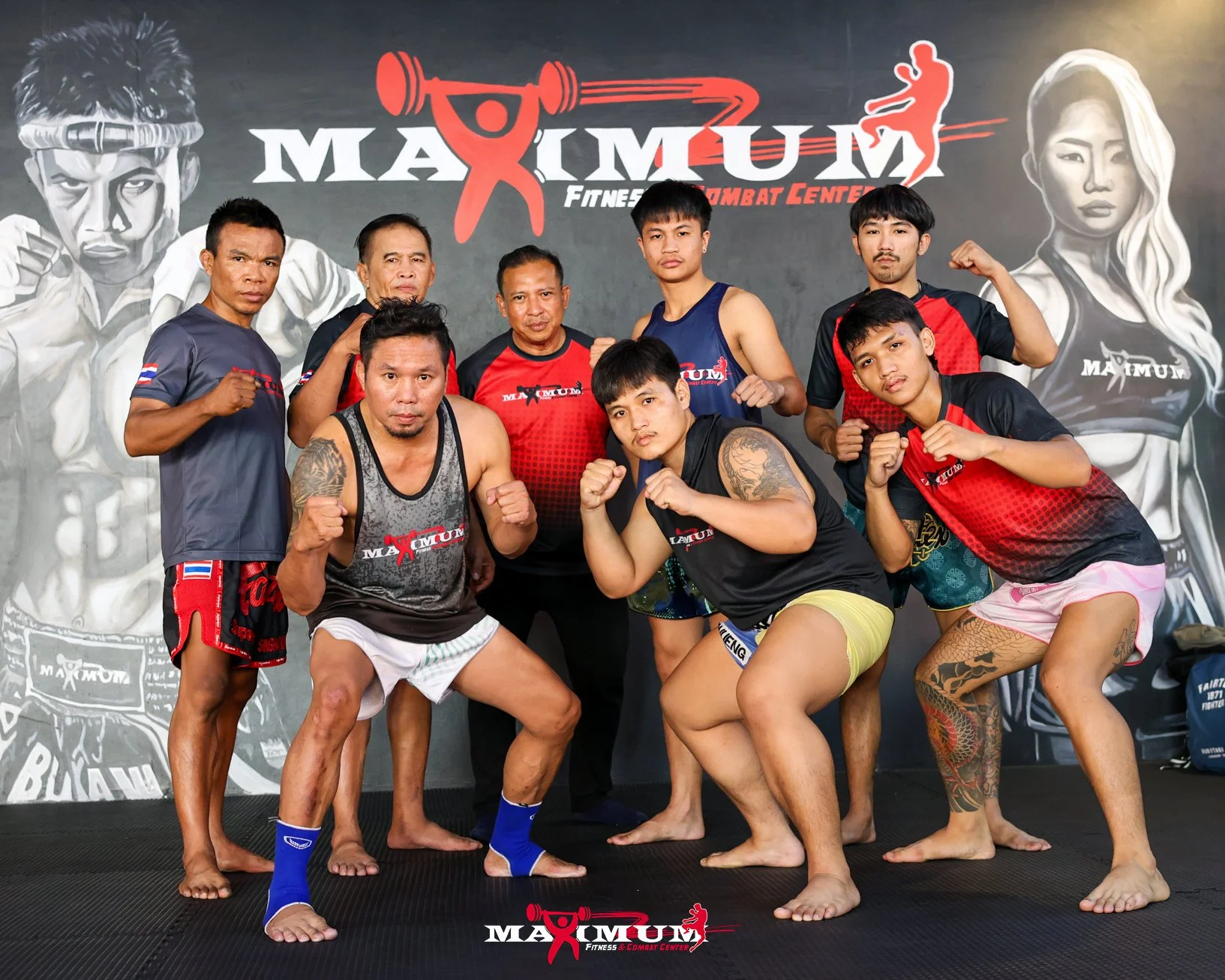 Group of men in martial arts attire posing in a gym with a gym-themed mural background.