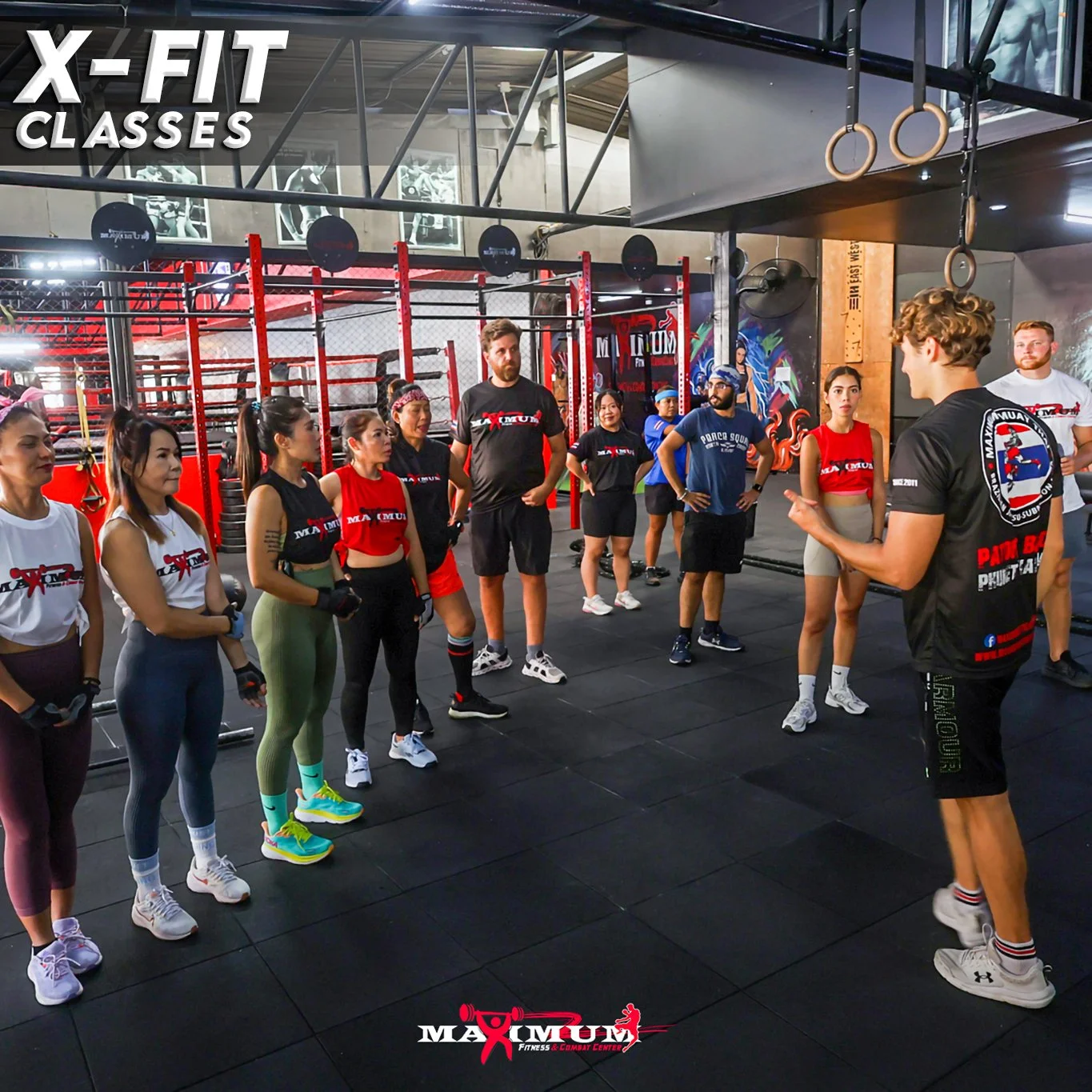 A group of people listening to a trainer in a gym with workout equipment and gymnastic rings.