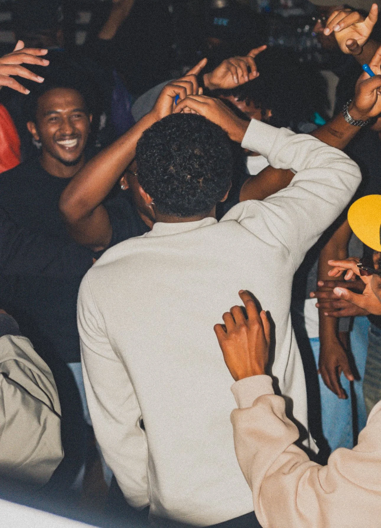 A group of people at a party, dancing and enjoying themselves, with one person in the center wrapping their arms around another person and everyone smiling or reaching out.